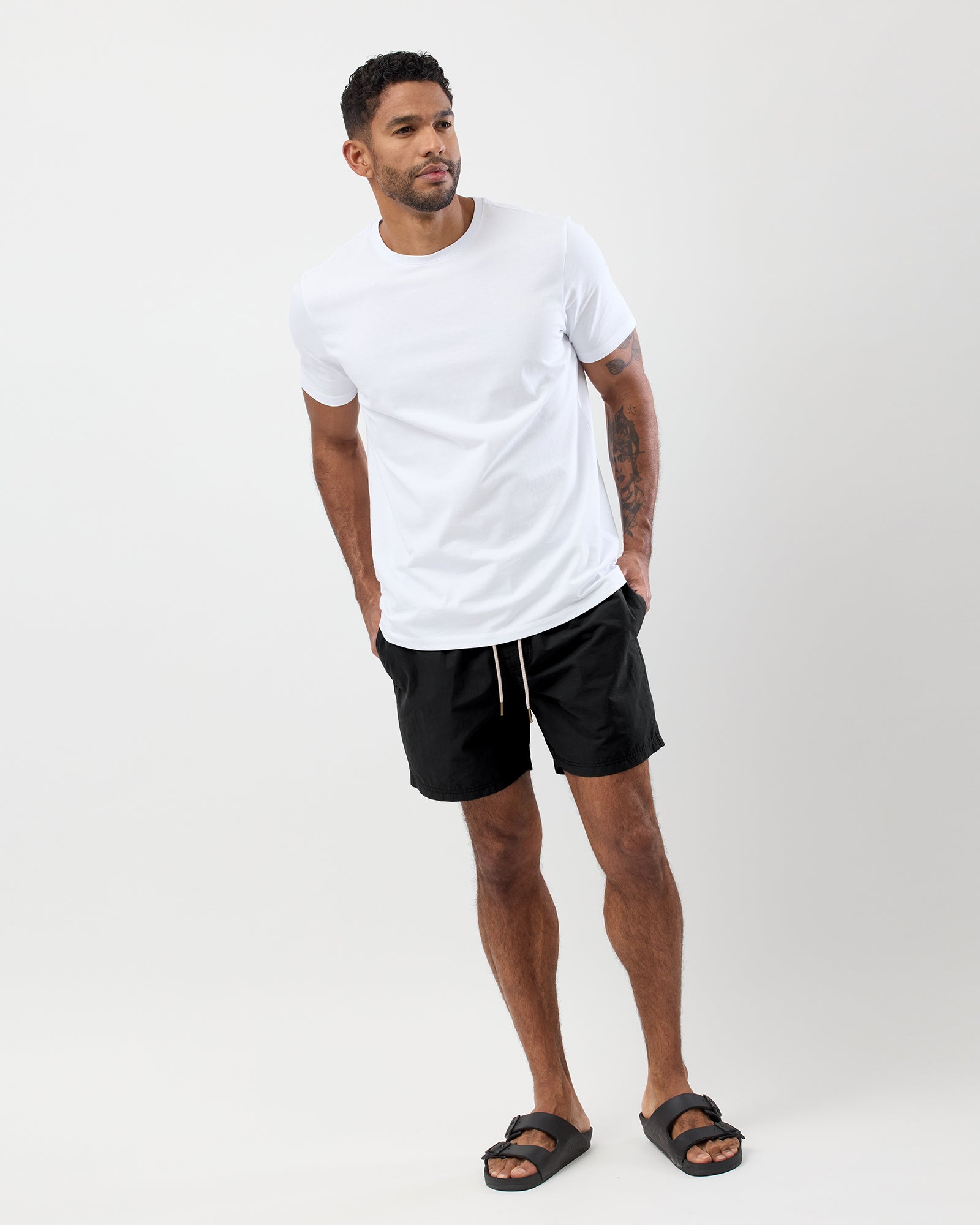 Man wearing a white t-shirt and black shorts with drawstring on a white background, full body image