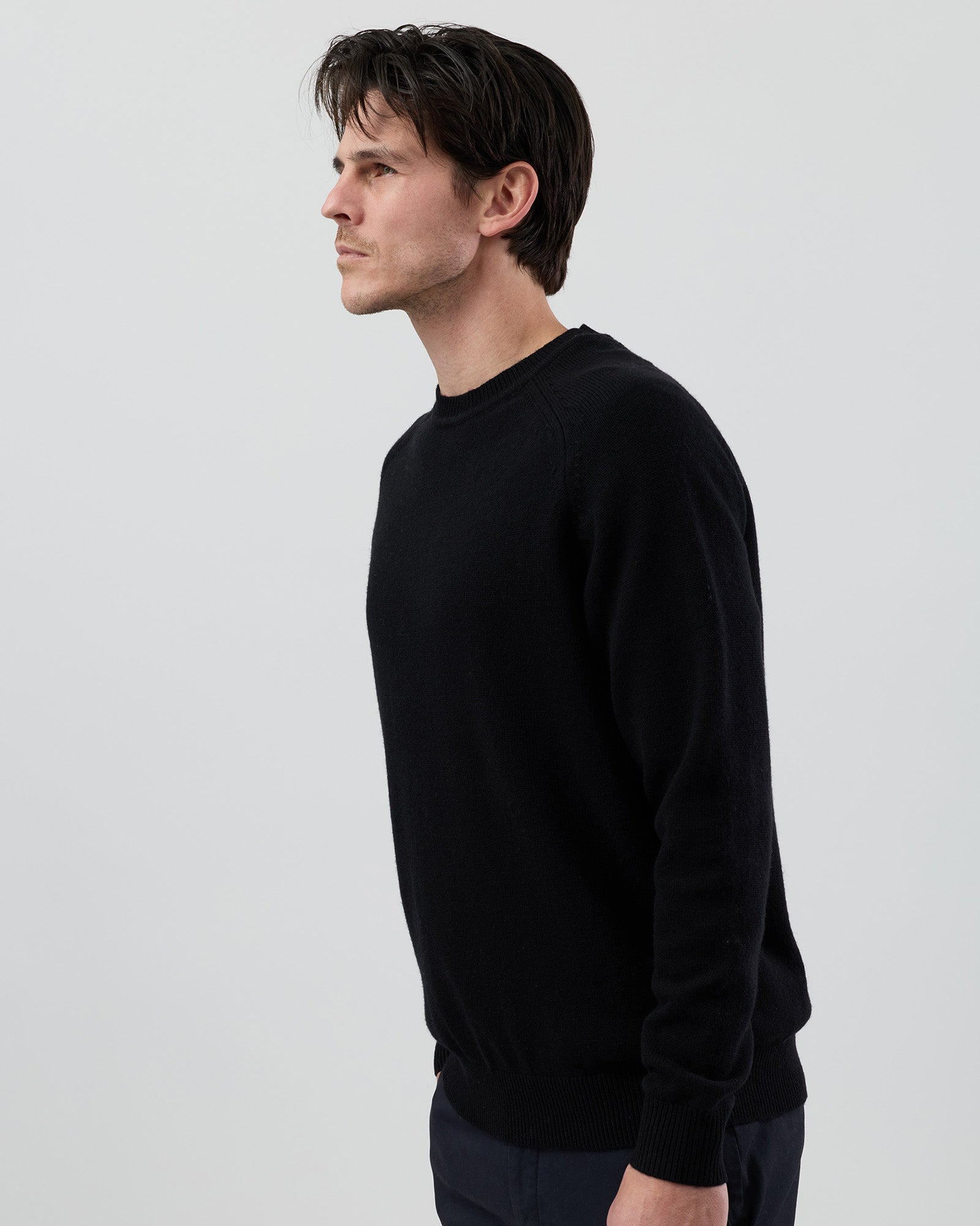 Angled side view of a men's black wool blend crew neck knit showing the tailored fit and premium fabric.