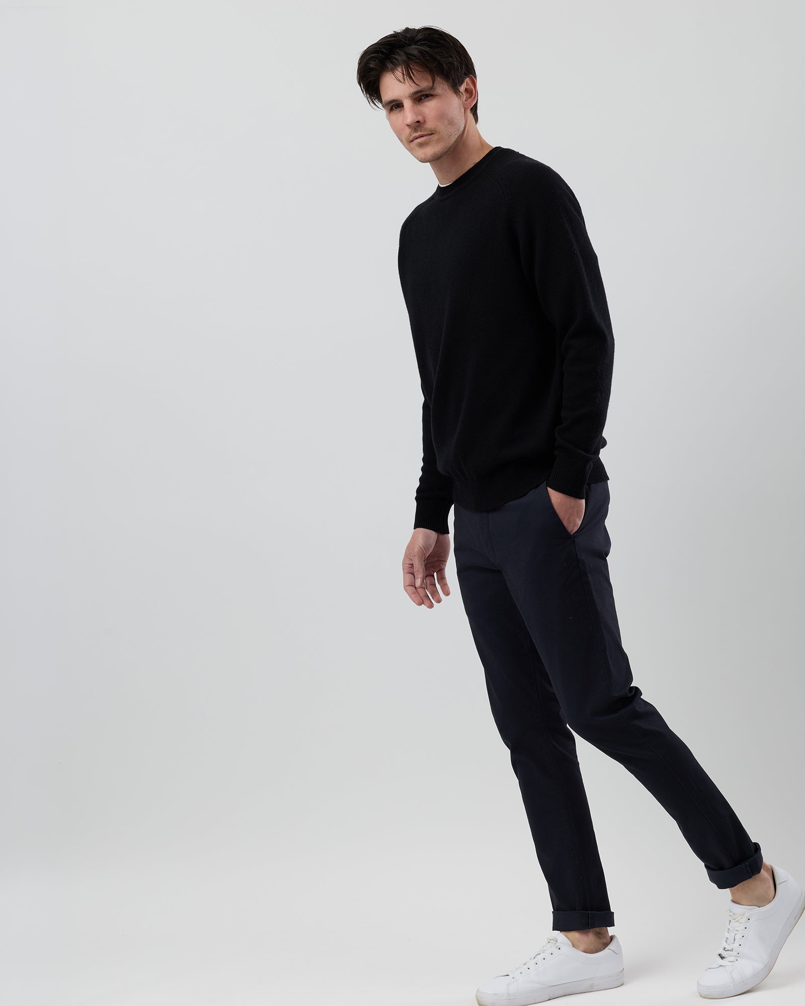 Full-length side profile of a men's black wool blend crew neck knit paired with navy chinos on a grey background.