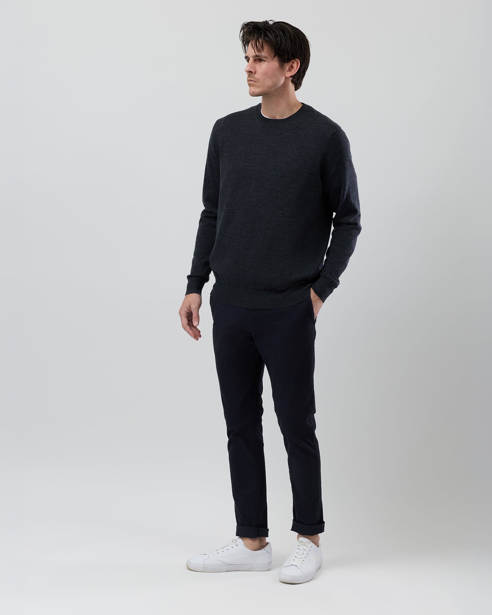 Side profile of a men's charcoal marl Australian ultrafine merino wool crew neck knit paired with navy chinos on a grey background by Wayvre Originals.