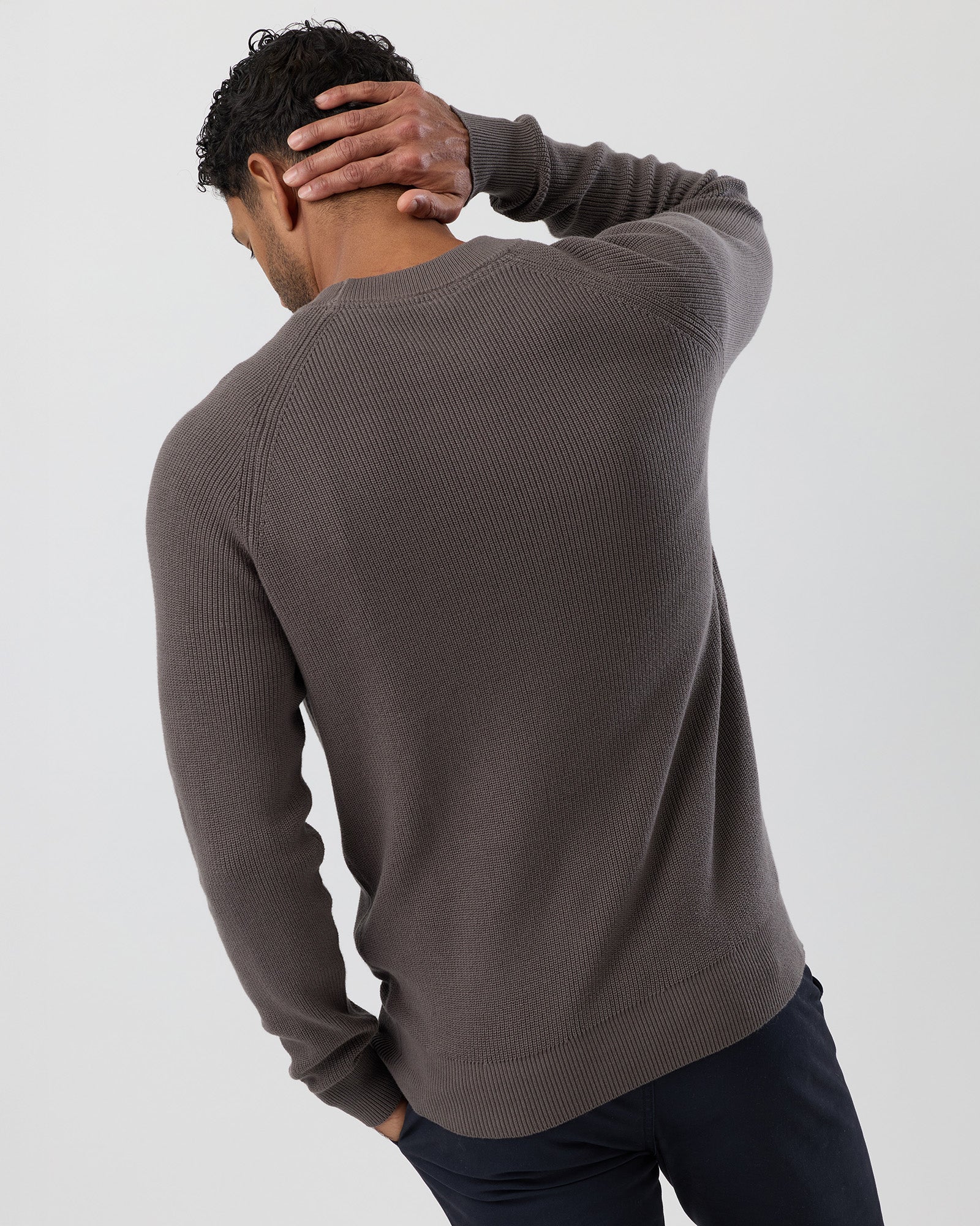 Man wearing a brown fisherman rib sweater against a plain background - rear view