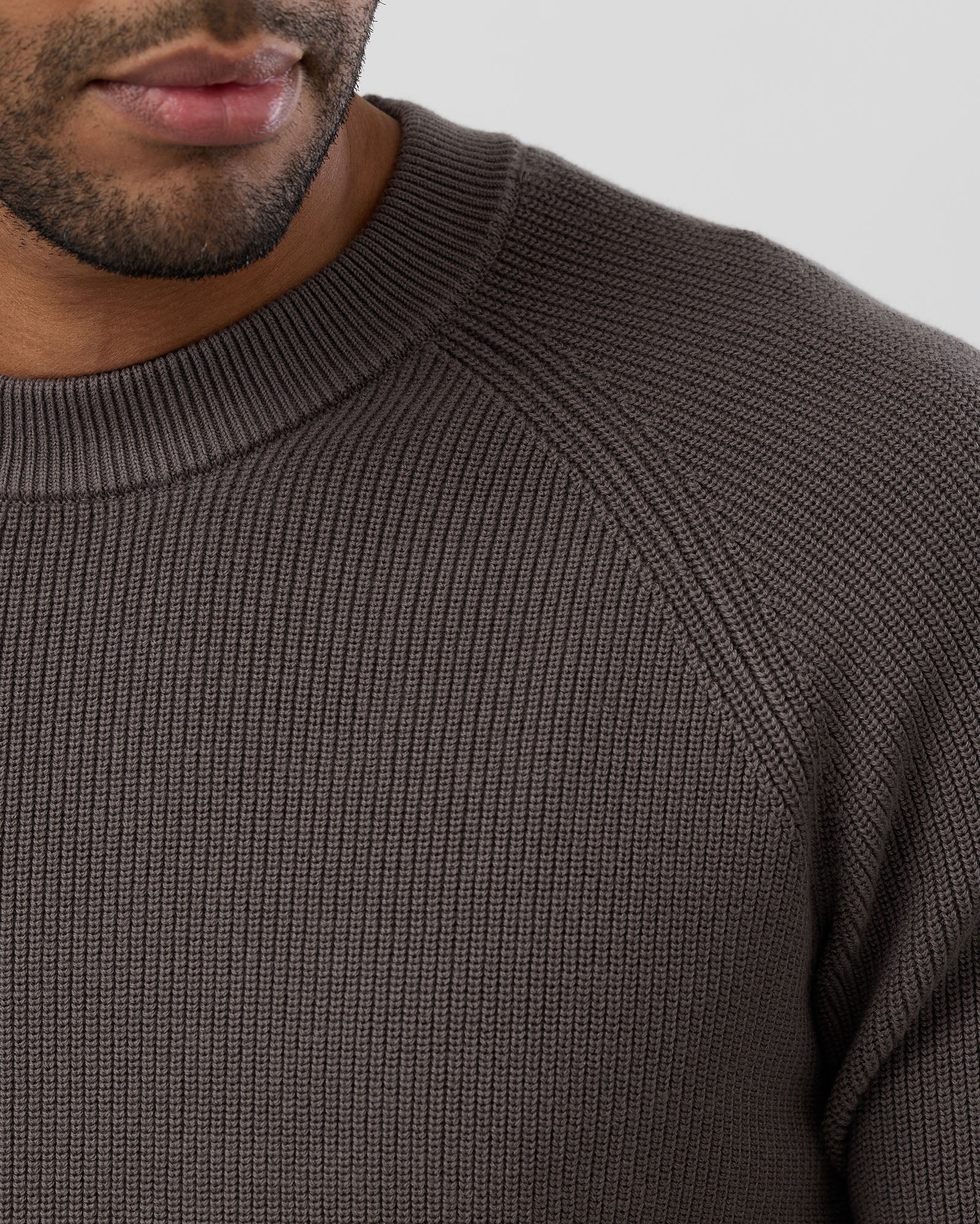Close-up of a person wearing a brown ribbed sweater against a neutral background