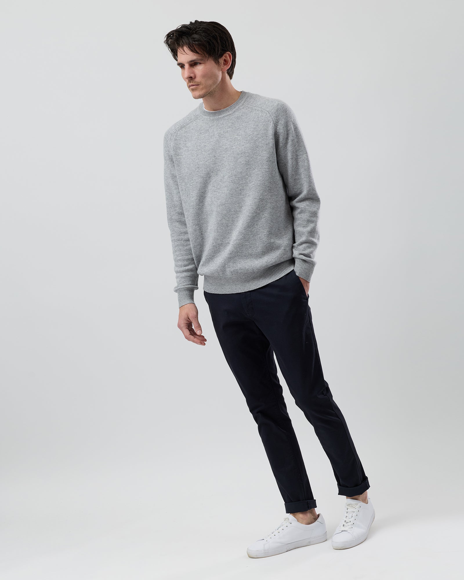 Full-length side profile of a men's light grey wool blend crew neck knit paired with navy chinos against a grey background.