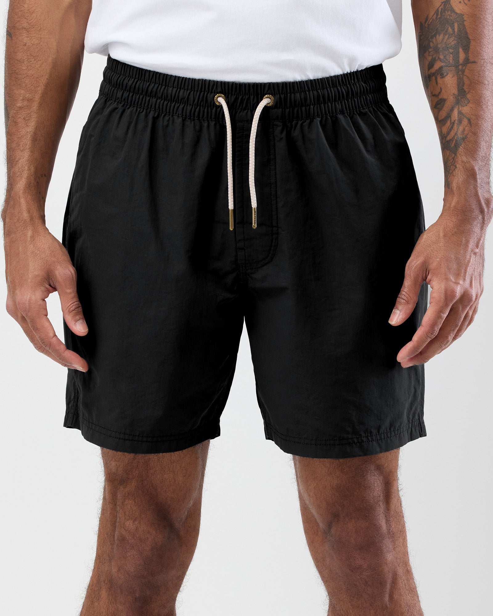 Person wearing black shorts with a white drawstring on a light gray background, close up shot