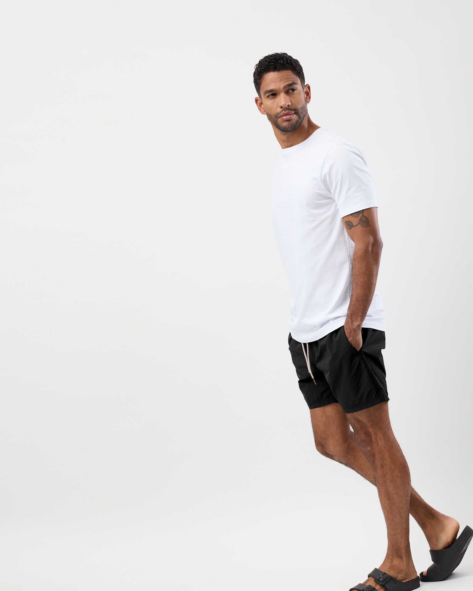 Man wearing a white Wayver t-shirt and black board shorts on a white background, full body view