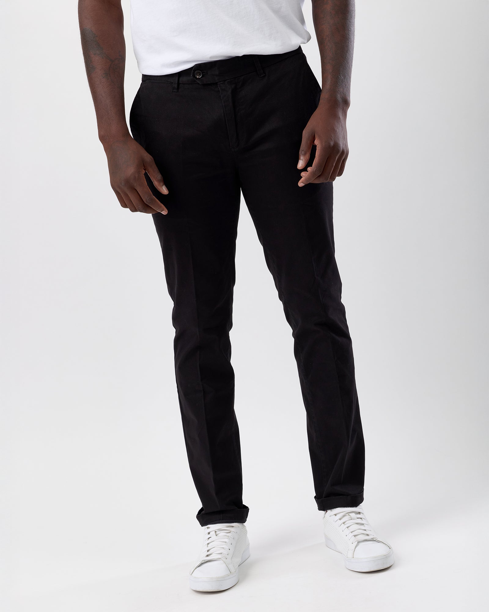 Person wearing black straight leg pants and white sneakers on a white background