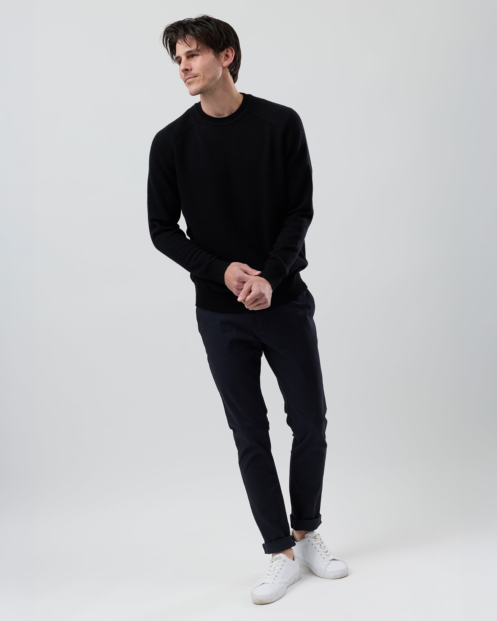 Full-length front view of a male model wearing the Wayver black wool blend crew neck knit with navy chinos against a grey background.