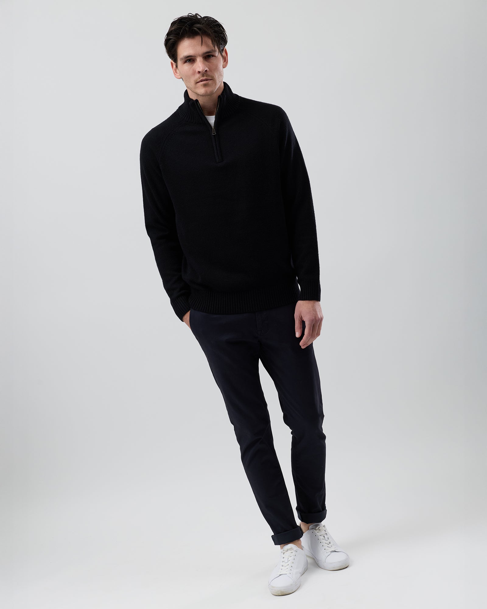 Full-length front view of a male model wearing the Wayver black wool blend half zip knit styled with navy chinos on a grey background.