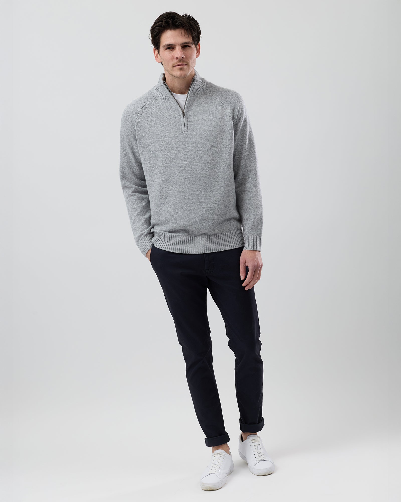 Full-length front view of a male model wearing the Wayver light grey wool blend half zip knit styled with navy chinos on a grey background.