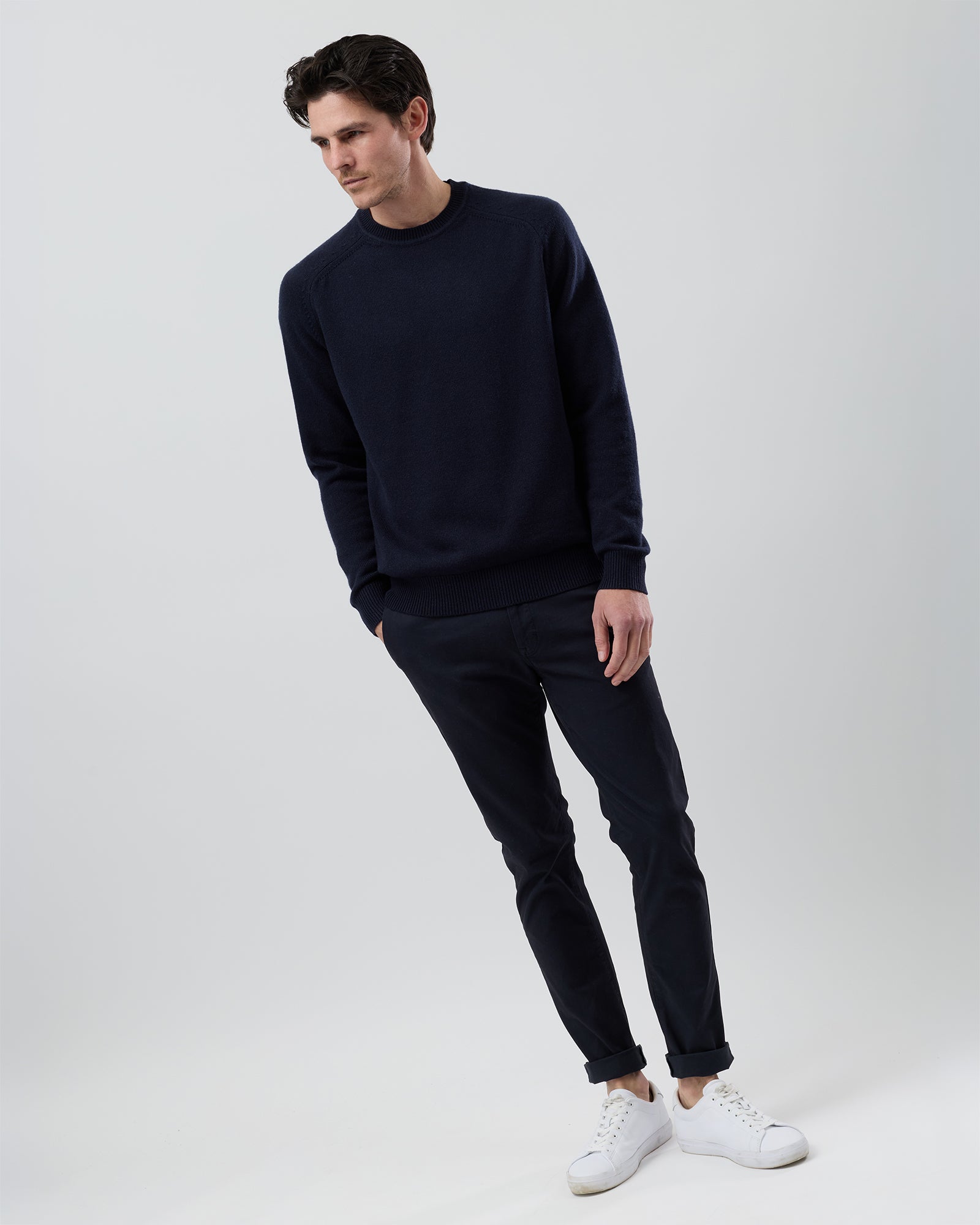 Full-length front view of a male model wearing the Wayver navy wool blend crew neck knit with navy chinos on a grey background.