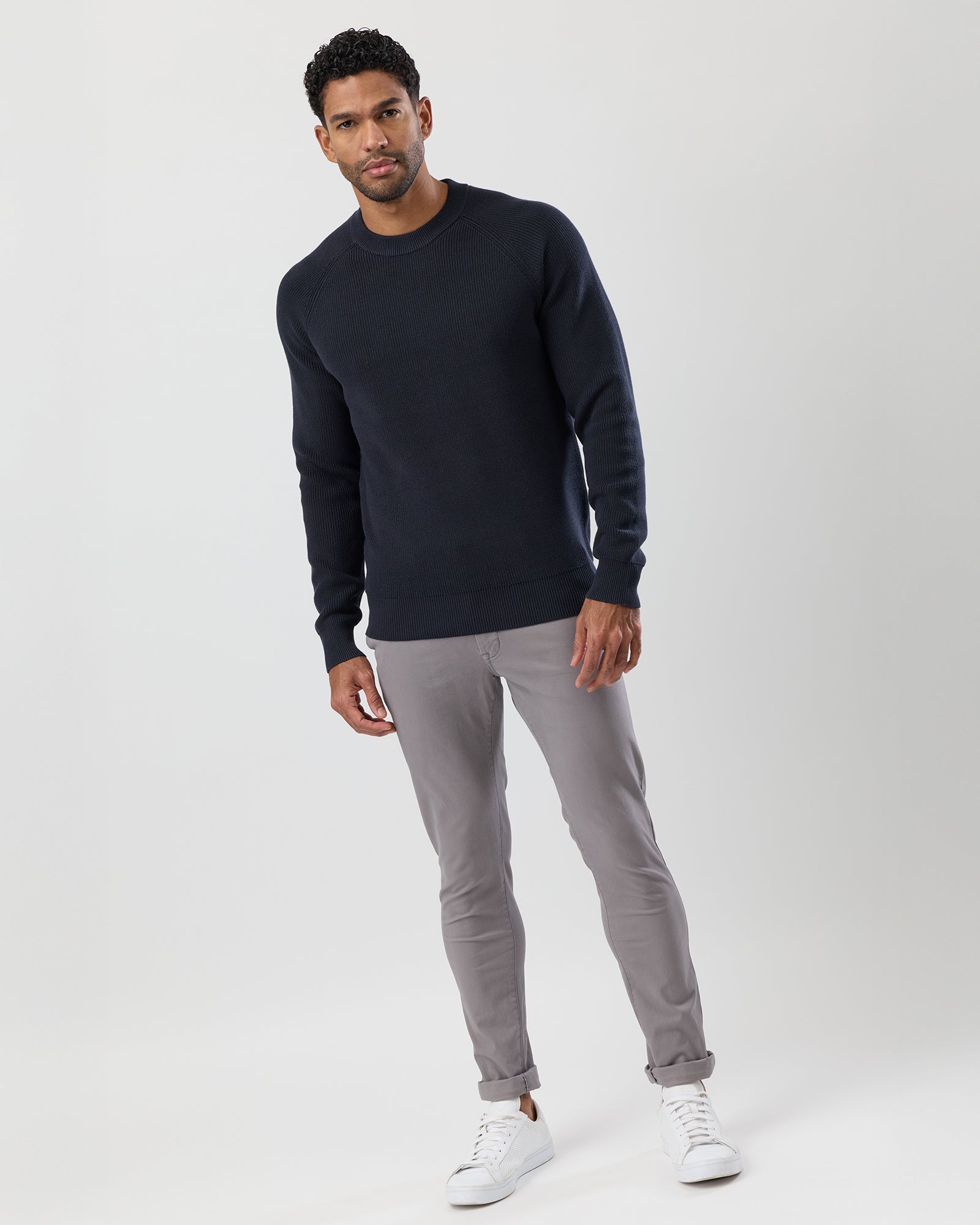 Man wearing a navy sweater and gray pants on a white background