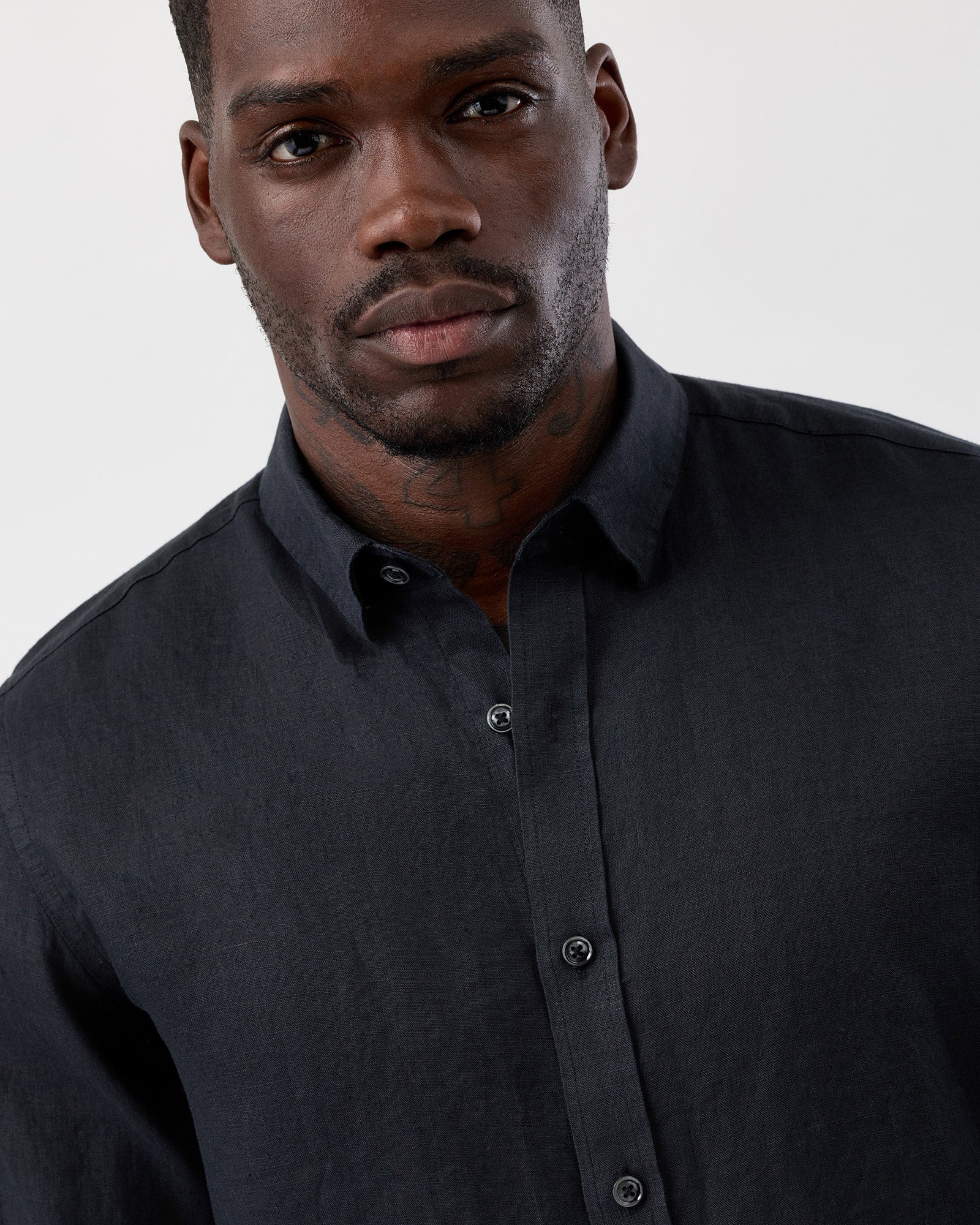 Close Up image of a man wearing a black wayver originals linen button-up shirt against a plain background