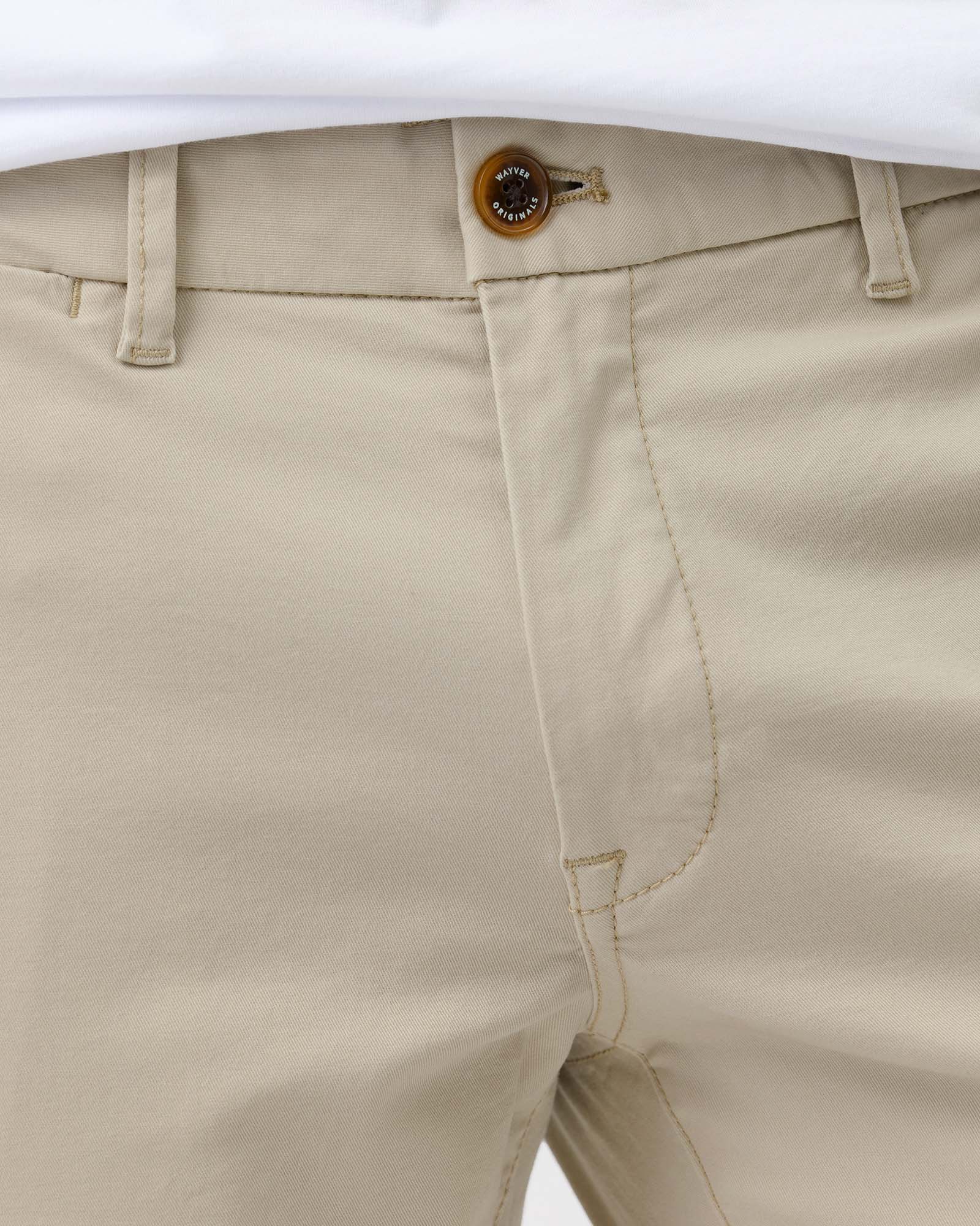 Close-up of Wayver Originals beige stretch cotton chinos showing the branded button, waistband, belt loops and cotton twill fabric.