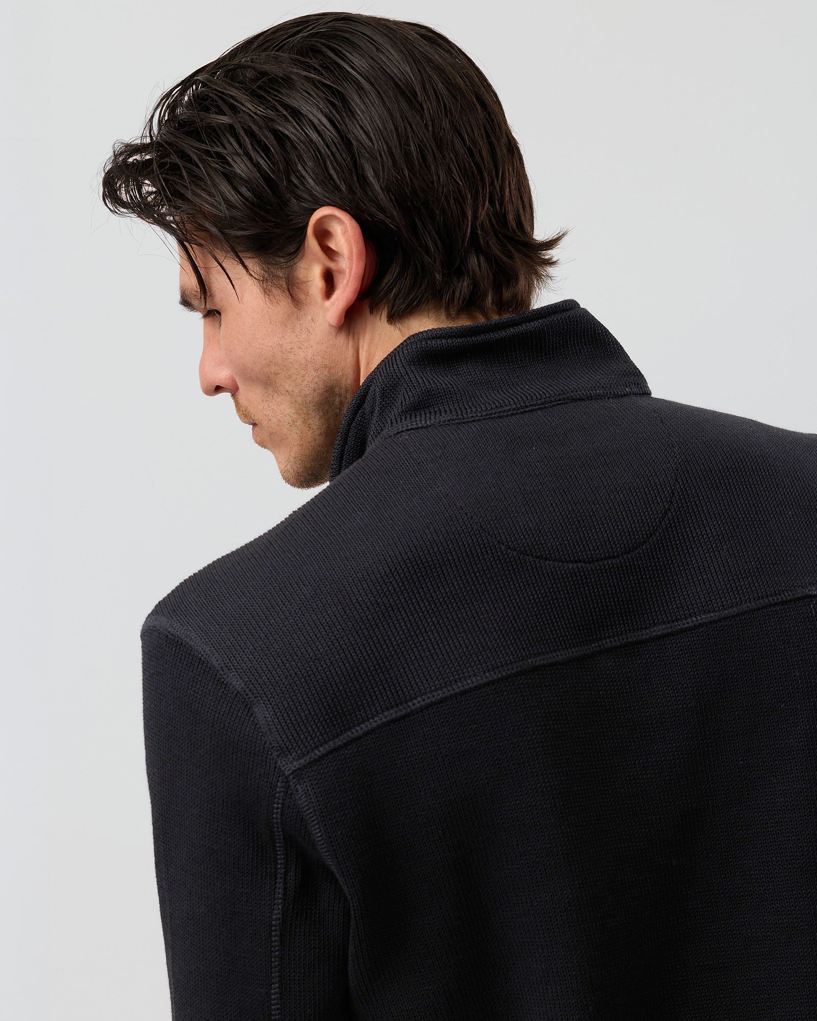 Close-up of men's black French rib knit pullover showing the textured cotton-rich fabric, raised collar and detailed shoulder seam construction.