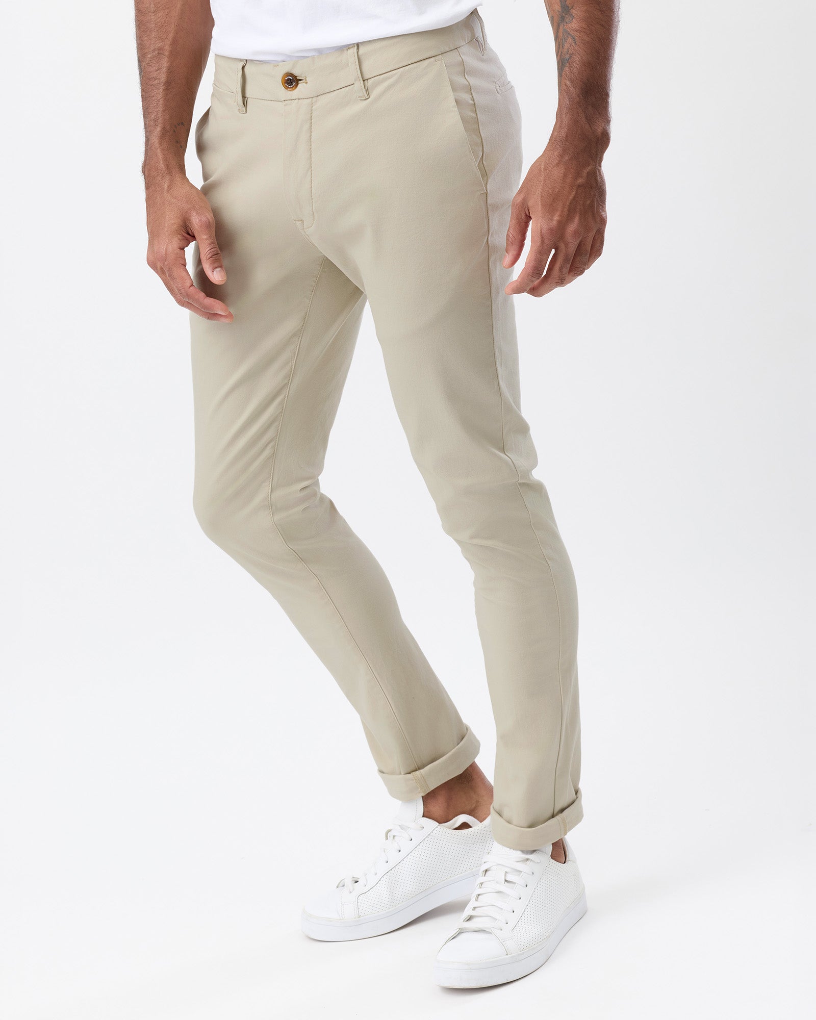 Angled view of men's beige stretch chino pants showing the slim tapered silhouette, side pockets and rolled hems.