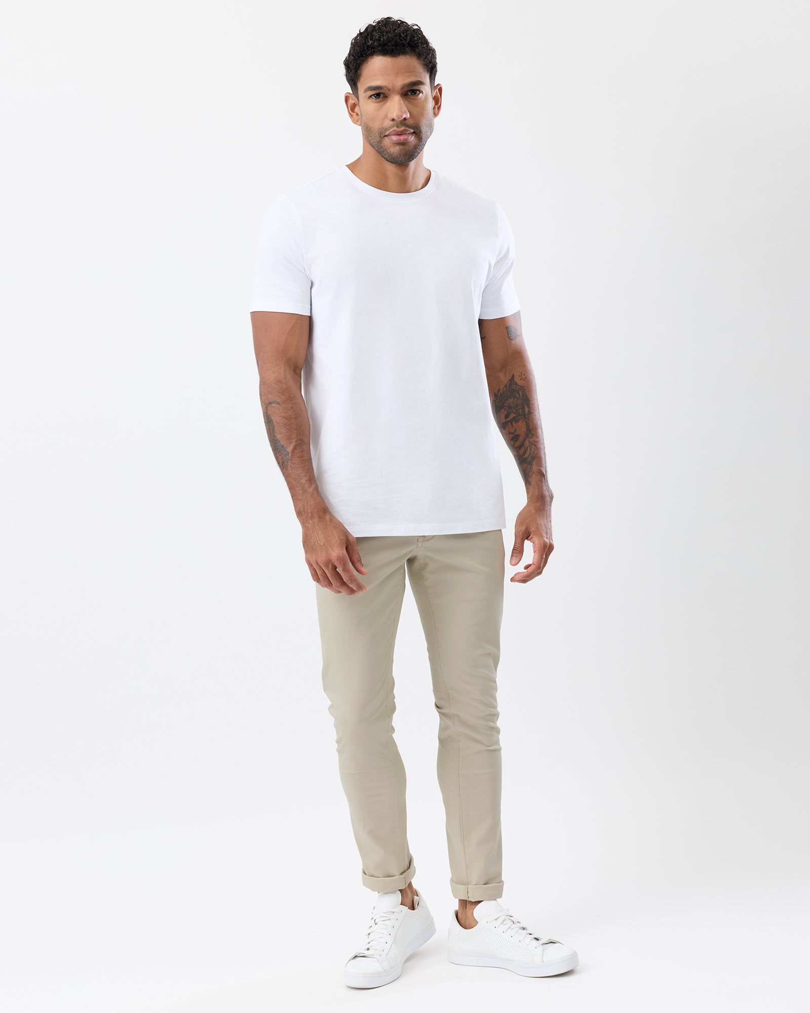 Model wearing men's beige slim stretch chinos by Wayver Originals, styled with a white crew neck t-shirt, white sneakers and rolled cuffs.