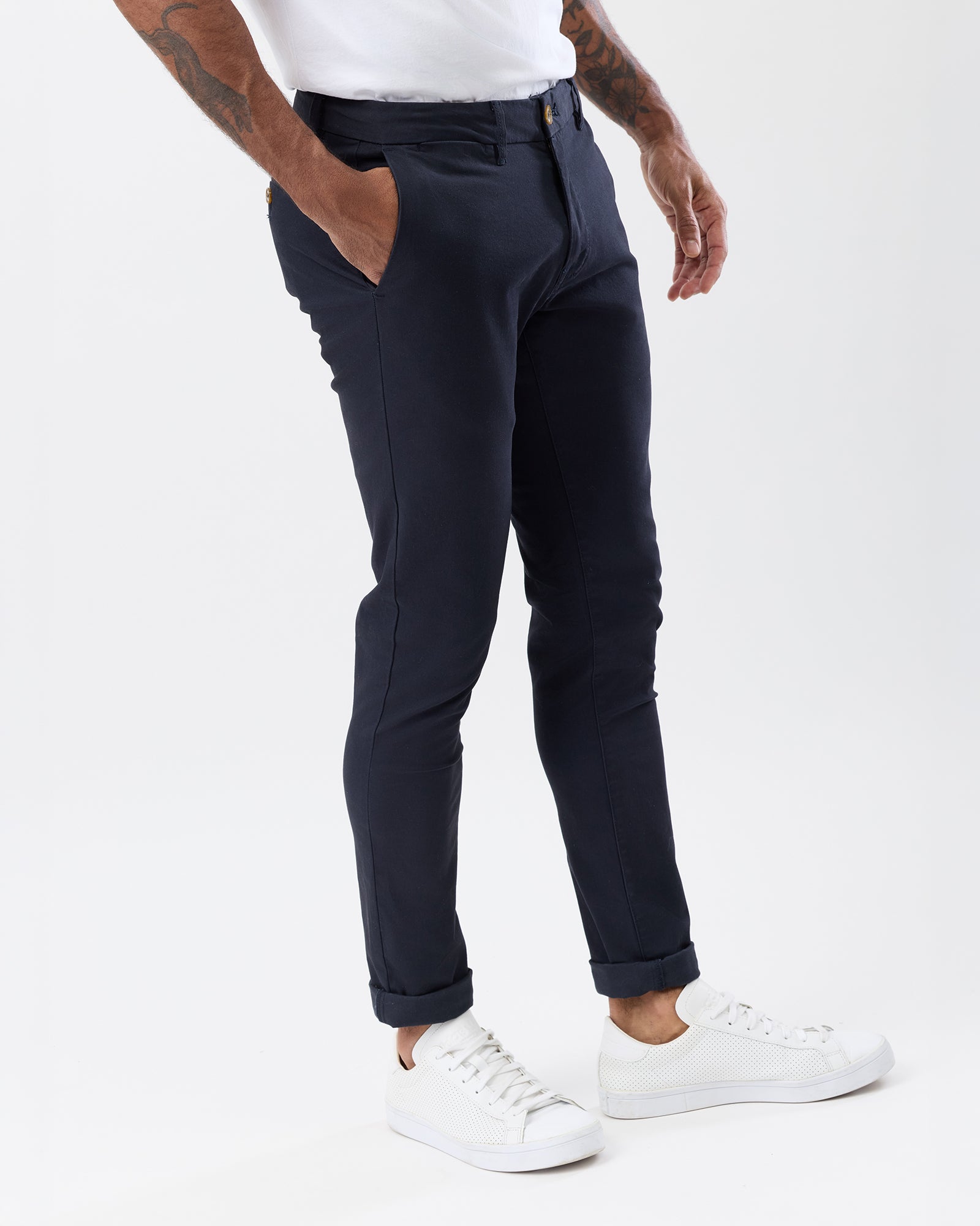 Angled view of men's navy stretch chino pants highlighting the slim tapered silhouette, side pockets and rolled cuffs.