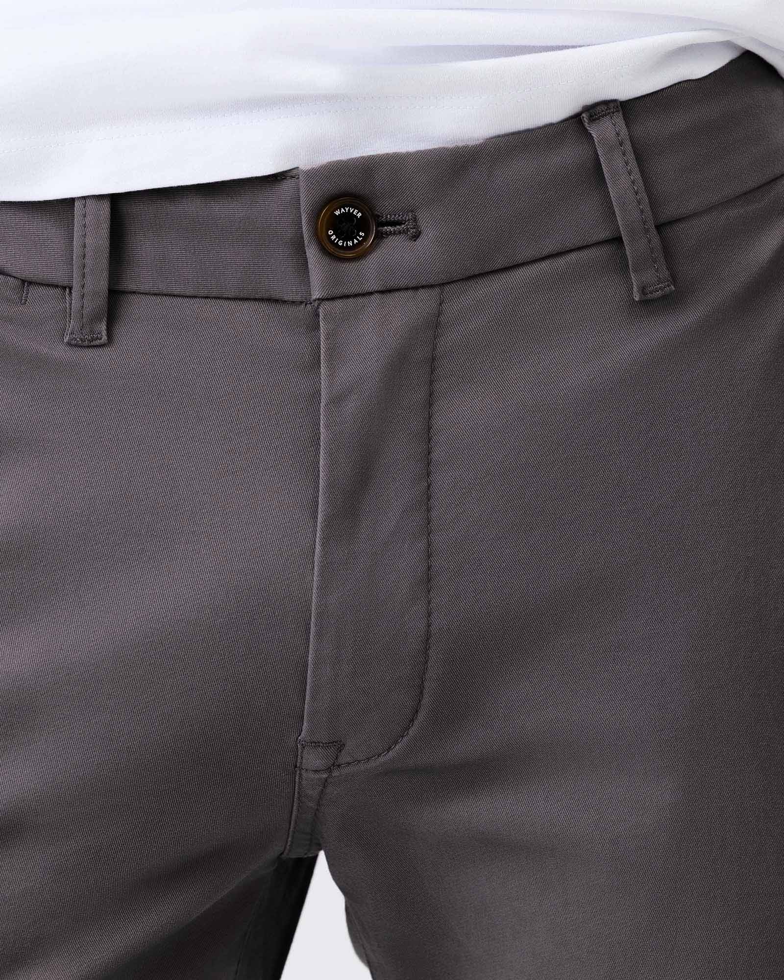 Close-up of smoke grey stretch cotton chinos showing the waistband, branded button, belt loops and cotton twill fabric.