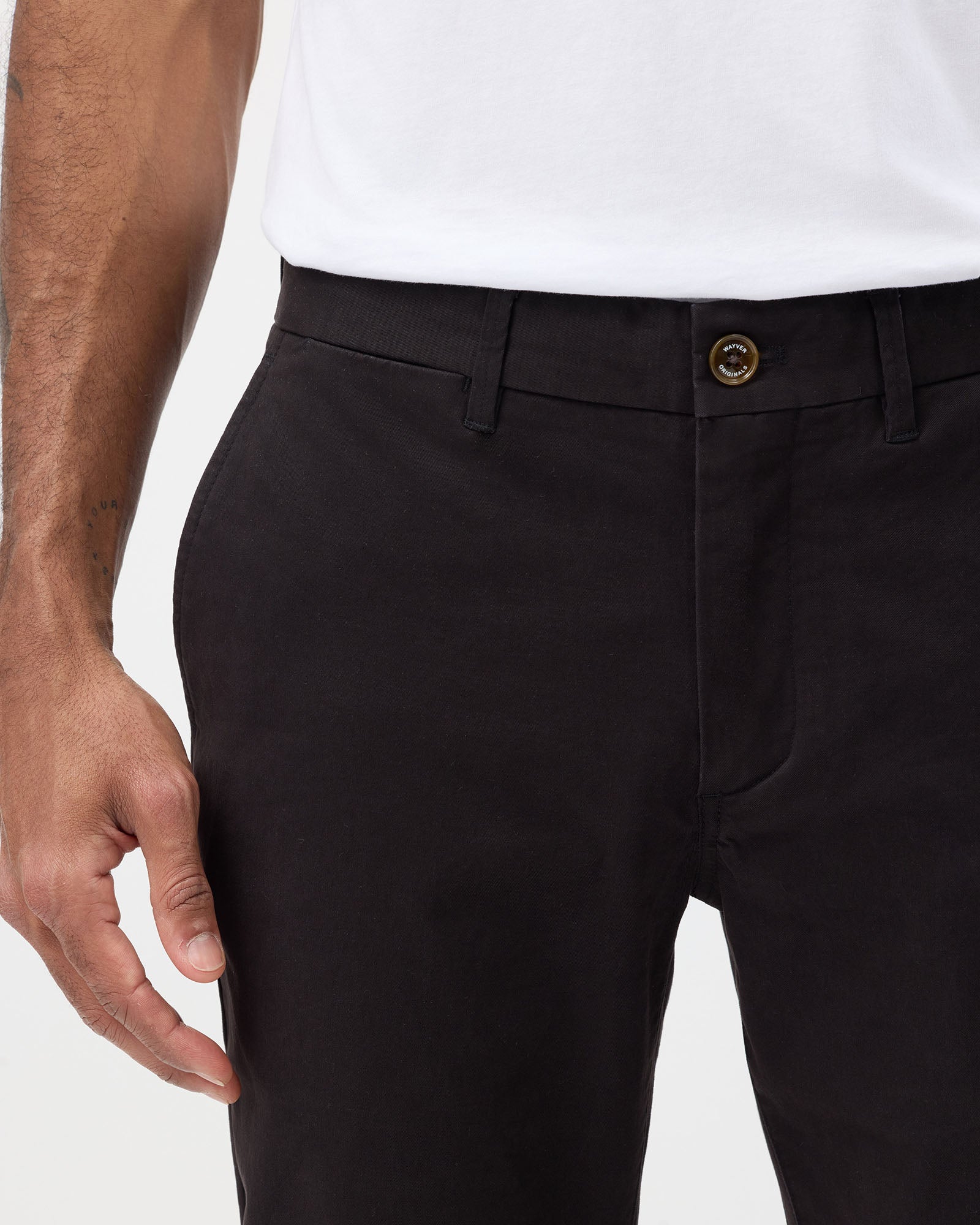 Close-up of Wayver Originals men's black slim stretch chinos showing waistband, branded button, belt loops and front pocket.