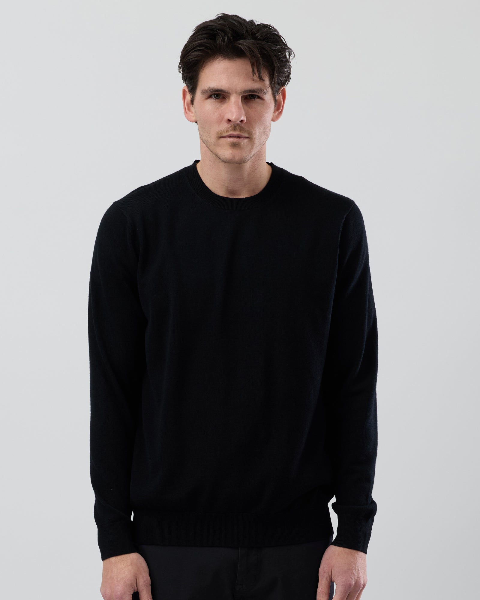 Close-up front image of a men's black Australian ultrafine merino wool crew neck sweater highlighting the fine gauge knit and premium fabric.