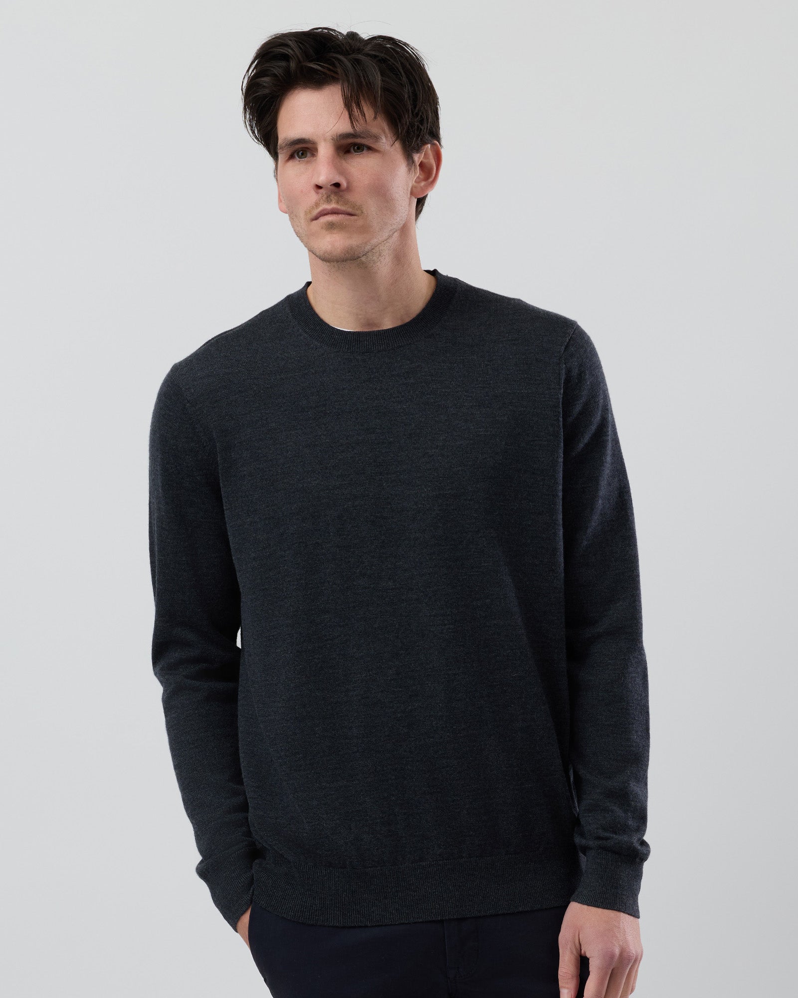 Male model wearing a charcoal marl Australian ultrafine merino wool crew neck knitted jumper on a grey background, front cropped view showing the fit and texture.