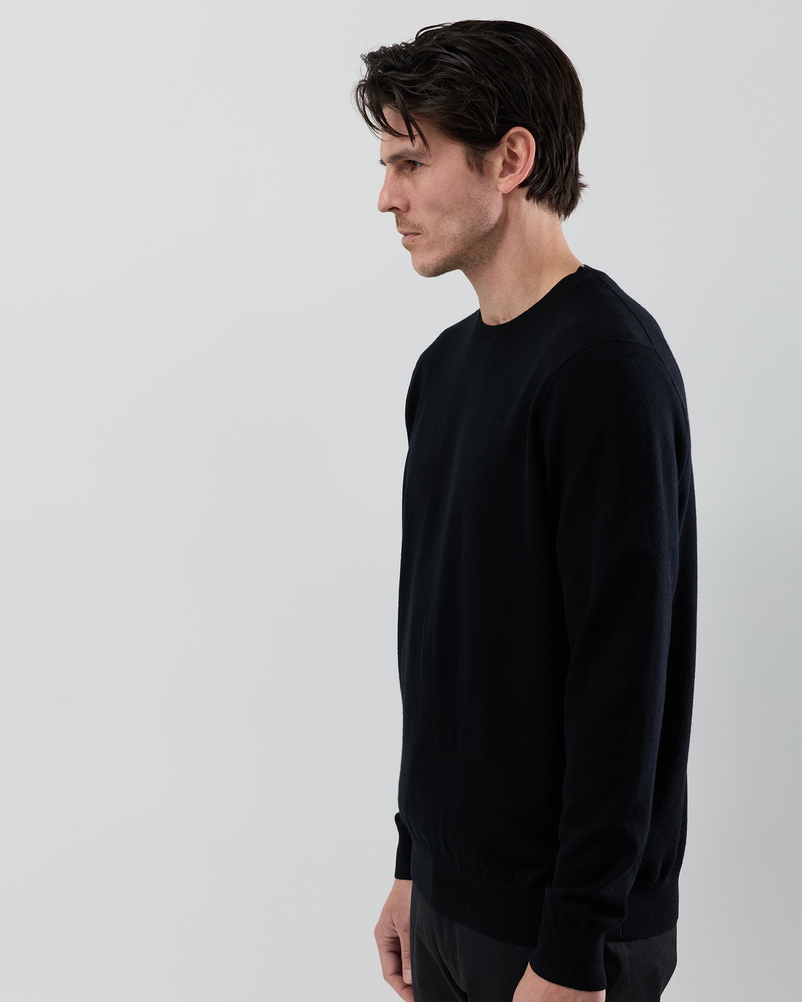 Angled side view of a men's black Australian ultrafine merino crew neck sweater highlighting the slim fit and premium wool construction.