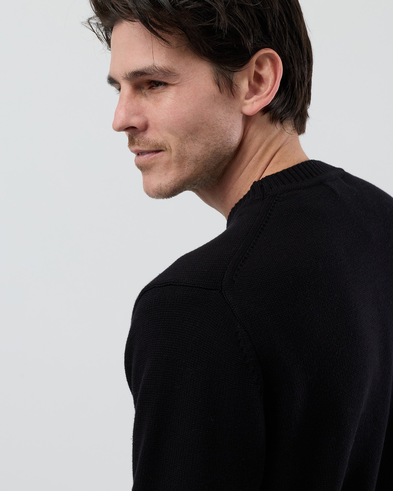Male model wearing the Wayver Essential Cotton Crew Neck Knit in black, front cropped view showing the regular fit and slim sleeve profile on a grey background.