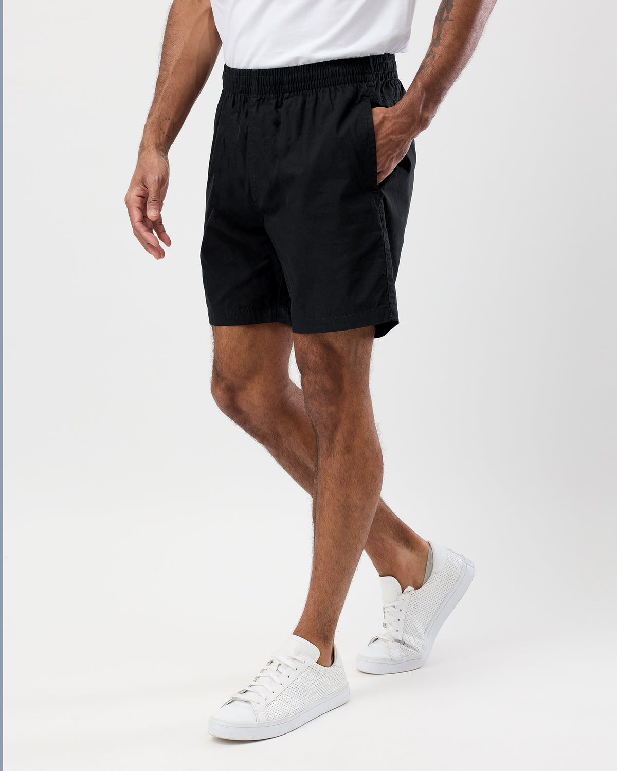 Person wearing black shorts and white sneakers on a white background, side view