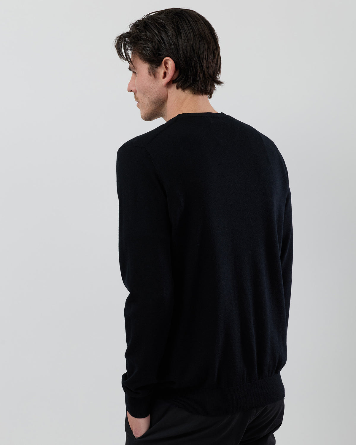 Rear view of a men's black Australian ultrafine merino wool knit showing the back fit and classic crew neck silhouette on a grey background.