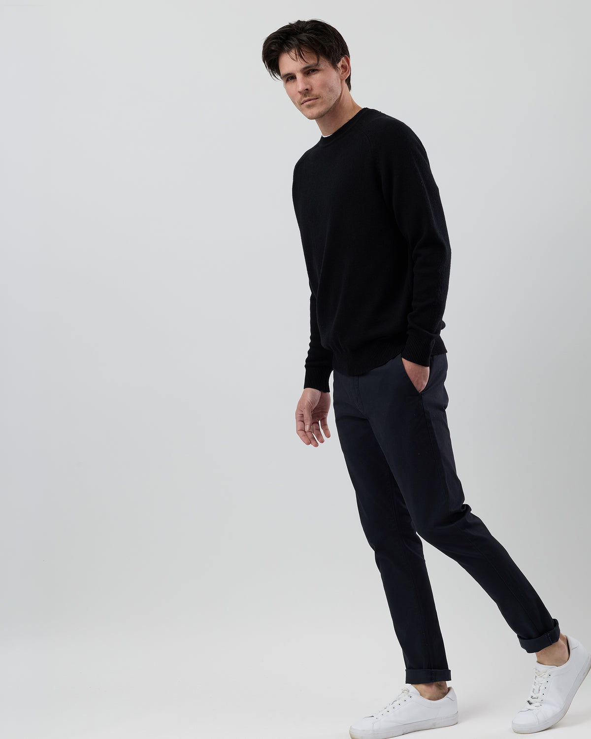 Full-length side profile of a men's black wool blend crew neck knit paired with navy chinos on a grey background.