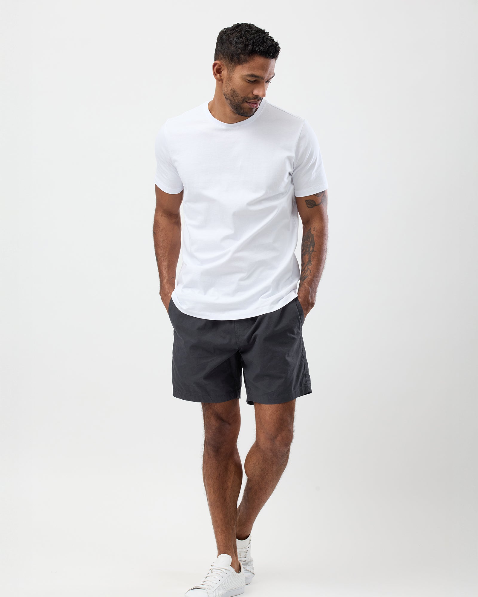 Man wearing a white t-shirt and dark shorts on a white background, full body shot