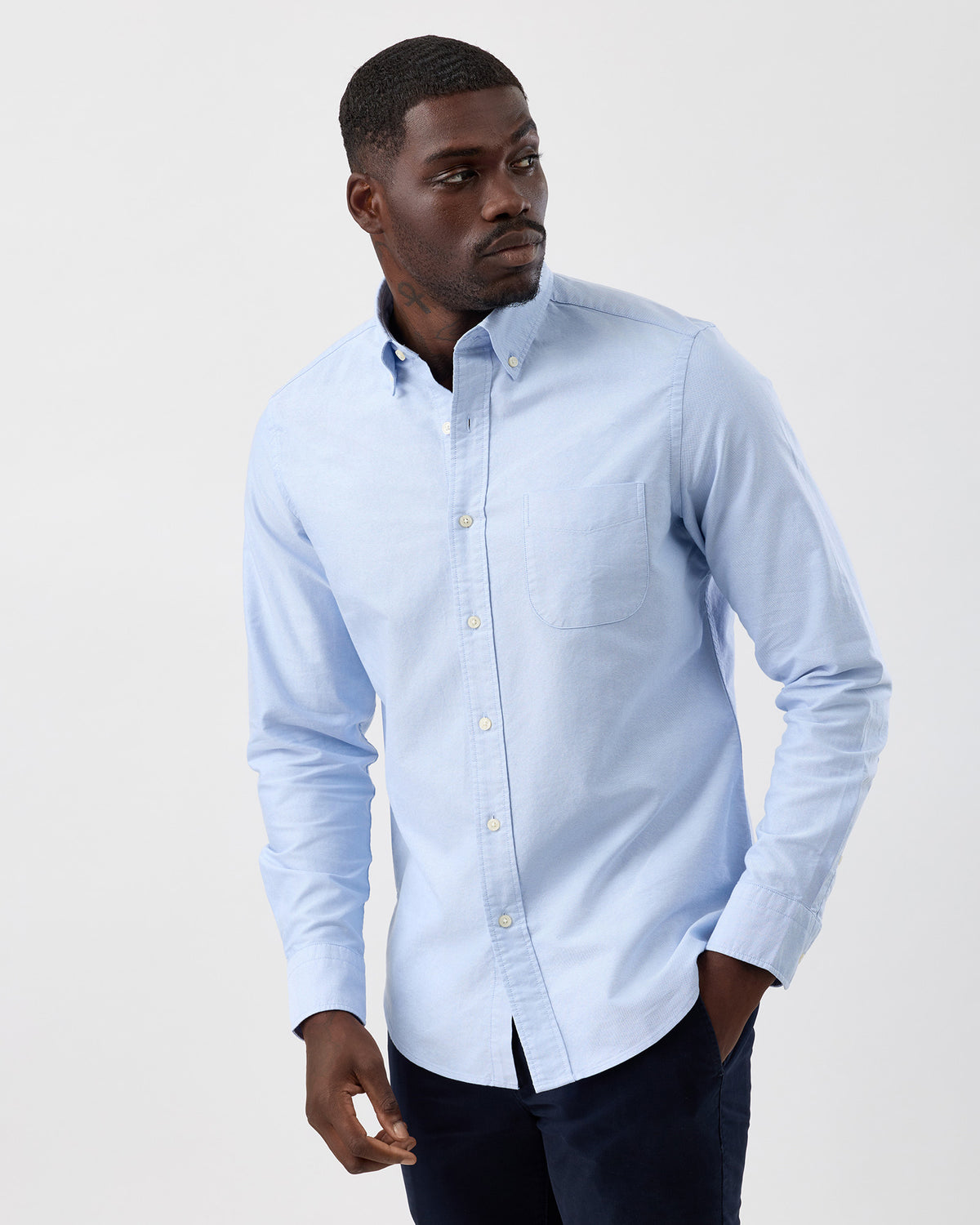 Man wearing a light blue cotton oxford button-up shirt with button-down collar against a plain background