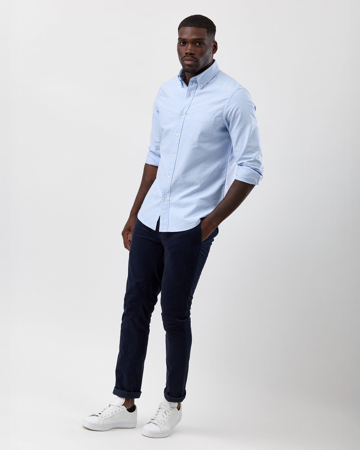 Man wearing a light blue wayver button-up shirt and dark pants on a white background