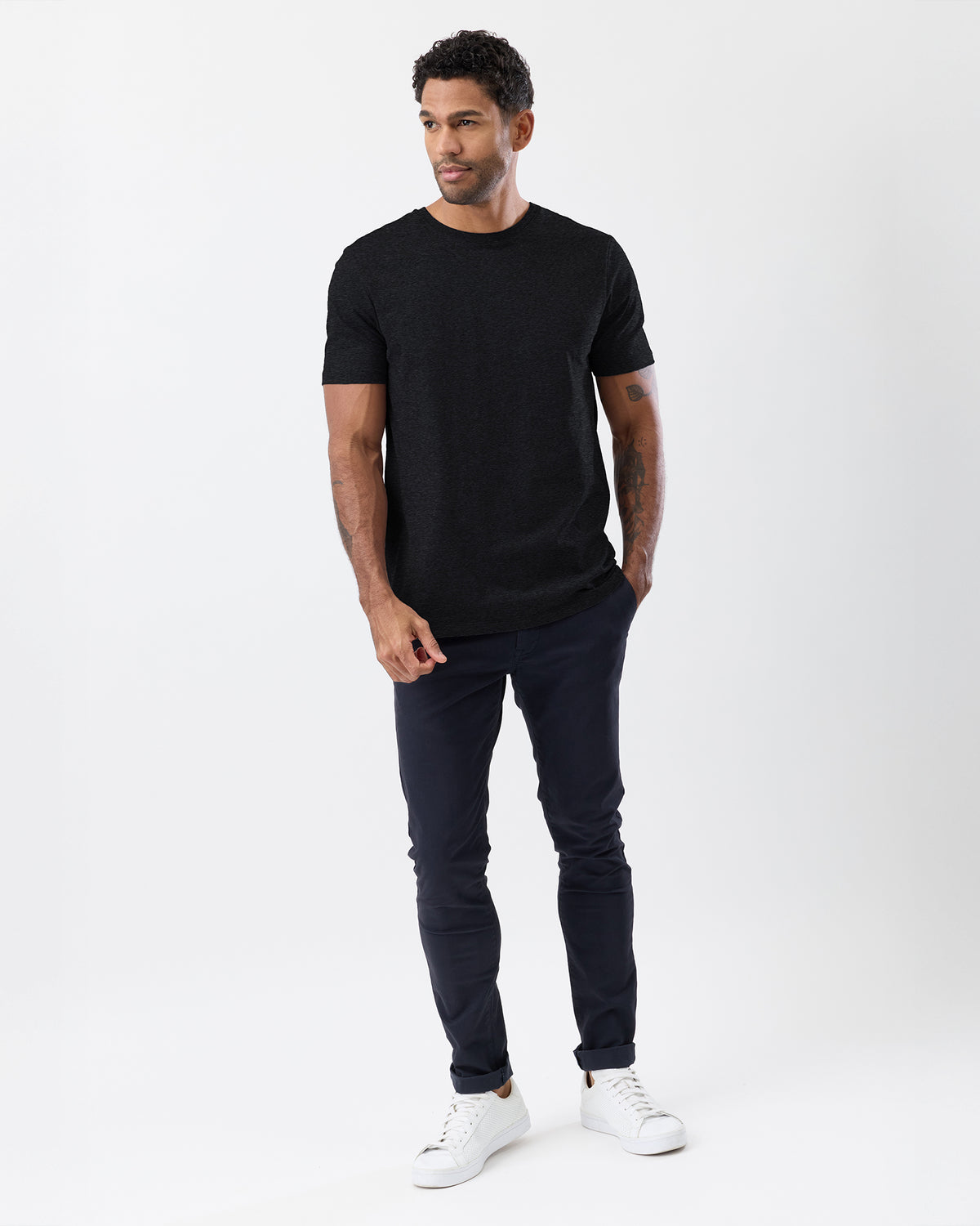 Man wearing a black t-shirt and dark jeans on a white background, with a slim fit