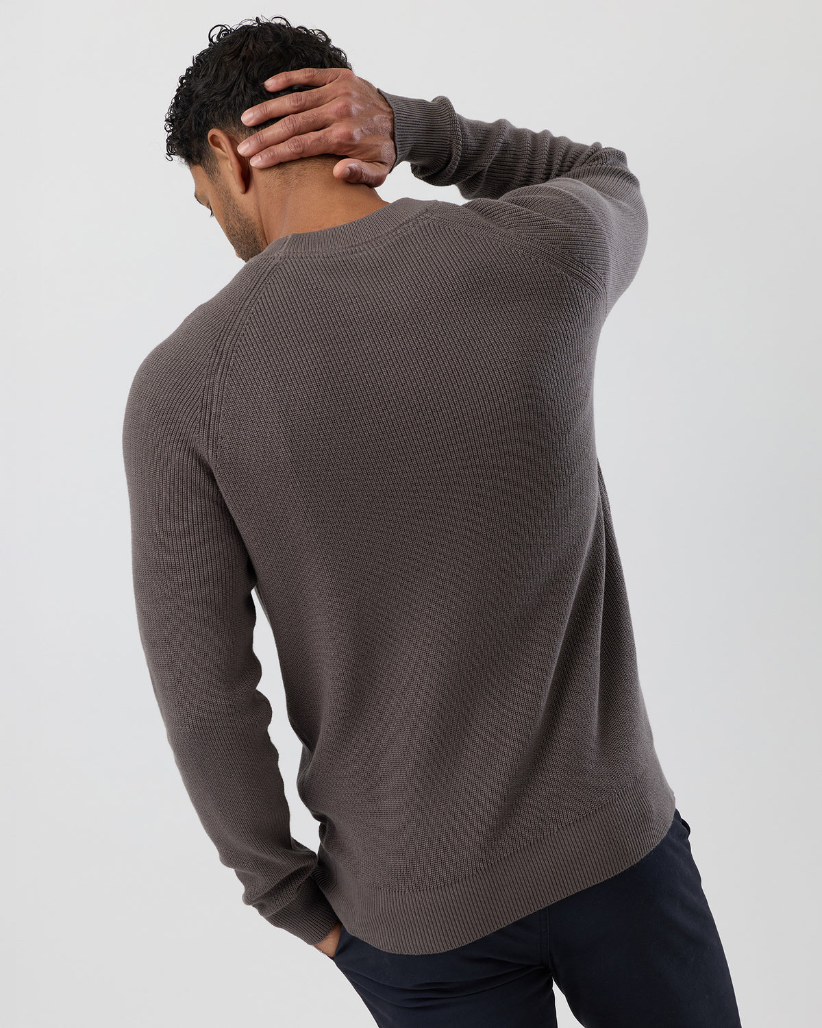 Man wearing a brown fisherman rib sweater against a plain background - rear view