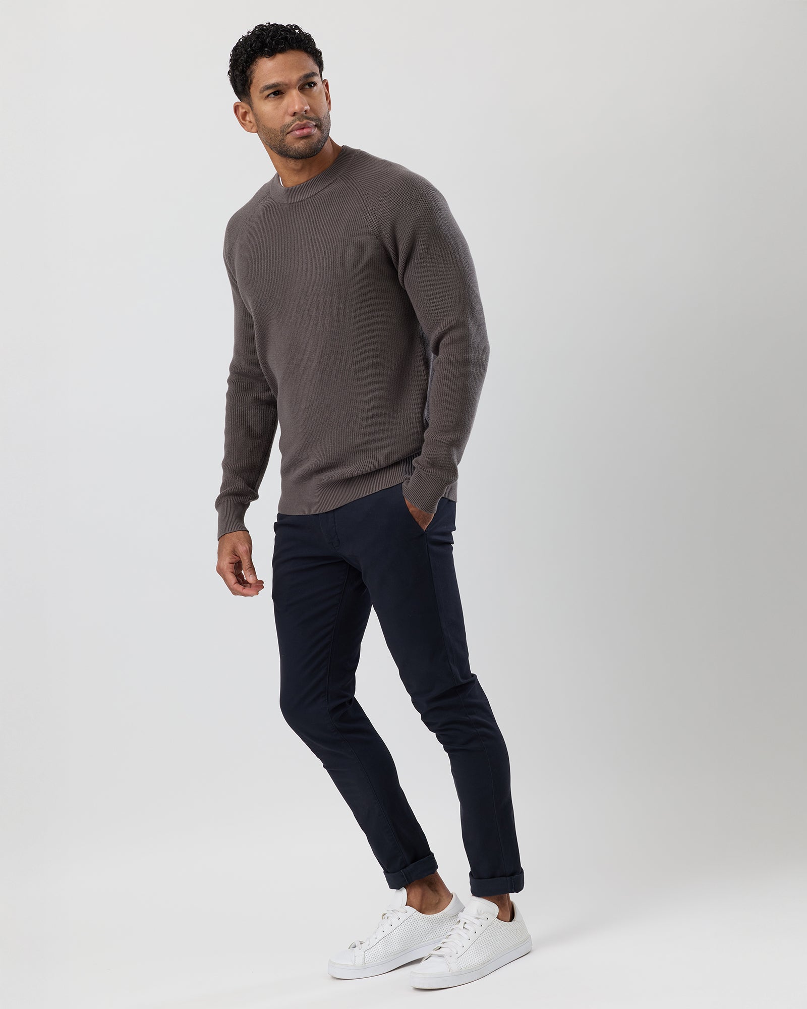 Man wearing a brown sweater and dark jeans on a white background, full body image