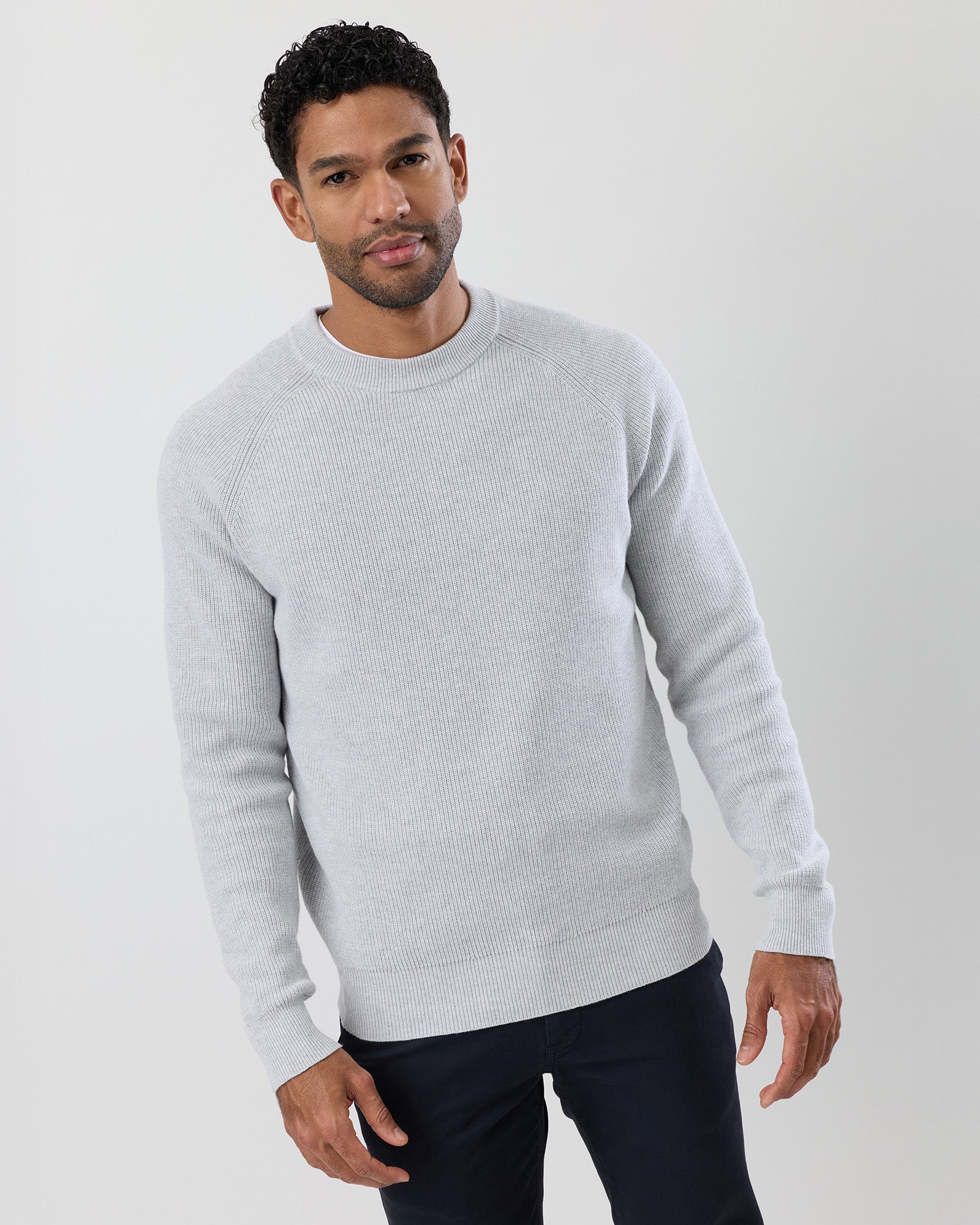 Close-up of a person wearing a light grey sweater against a neutral background