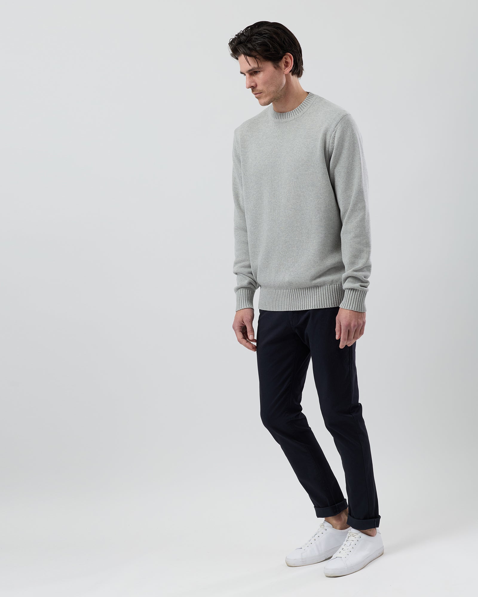 Side profile of a male model wearing the Wayver light grey cotton crew neck jumper with navy chinos showing the comfortable everyday fit.