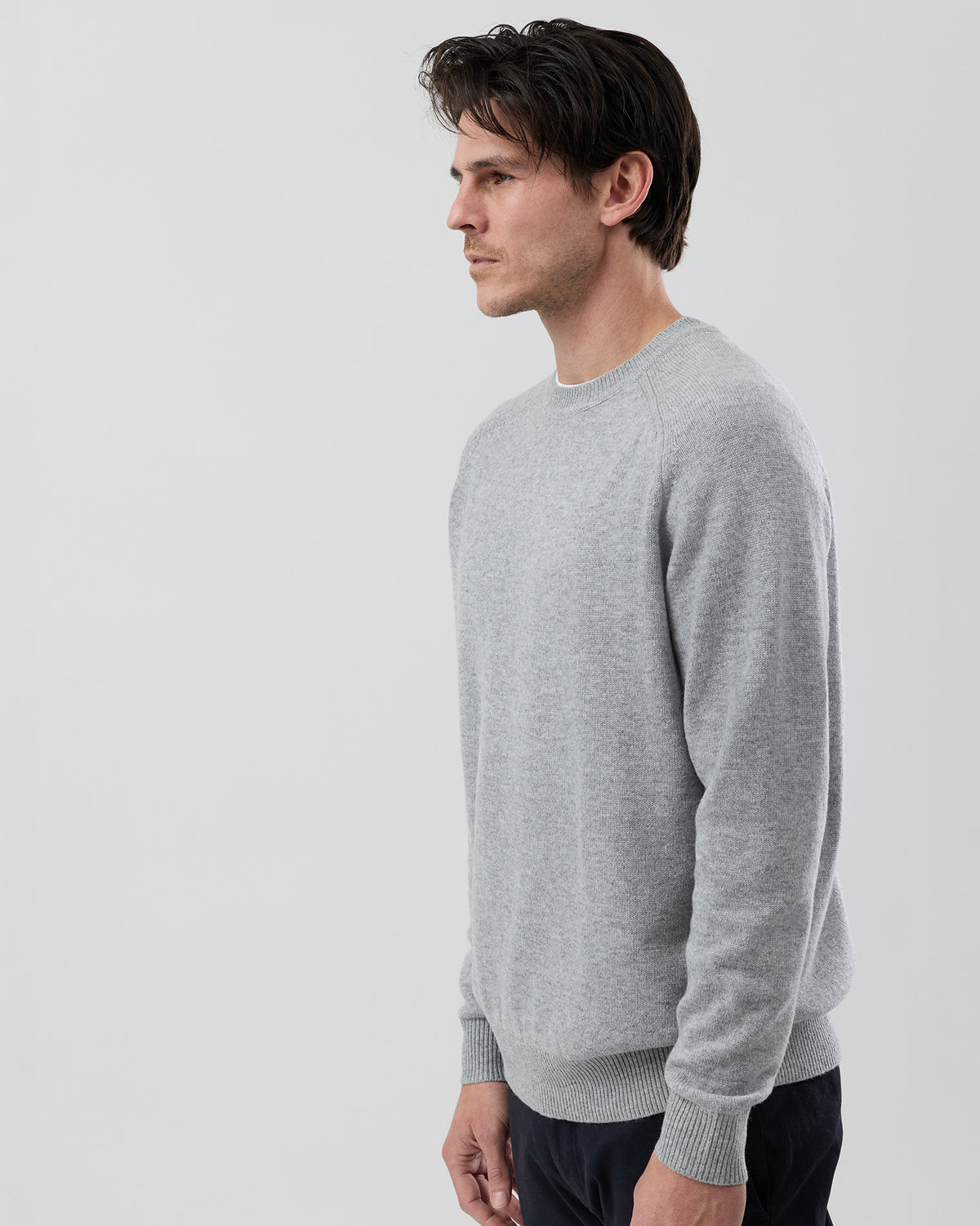 Angled side view of a men's light grey wool blend crew neck knit showing the tailored fit and premium knit construction.