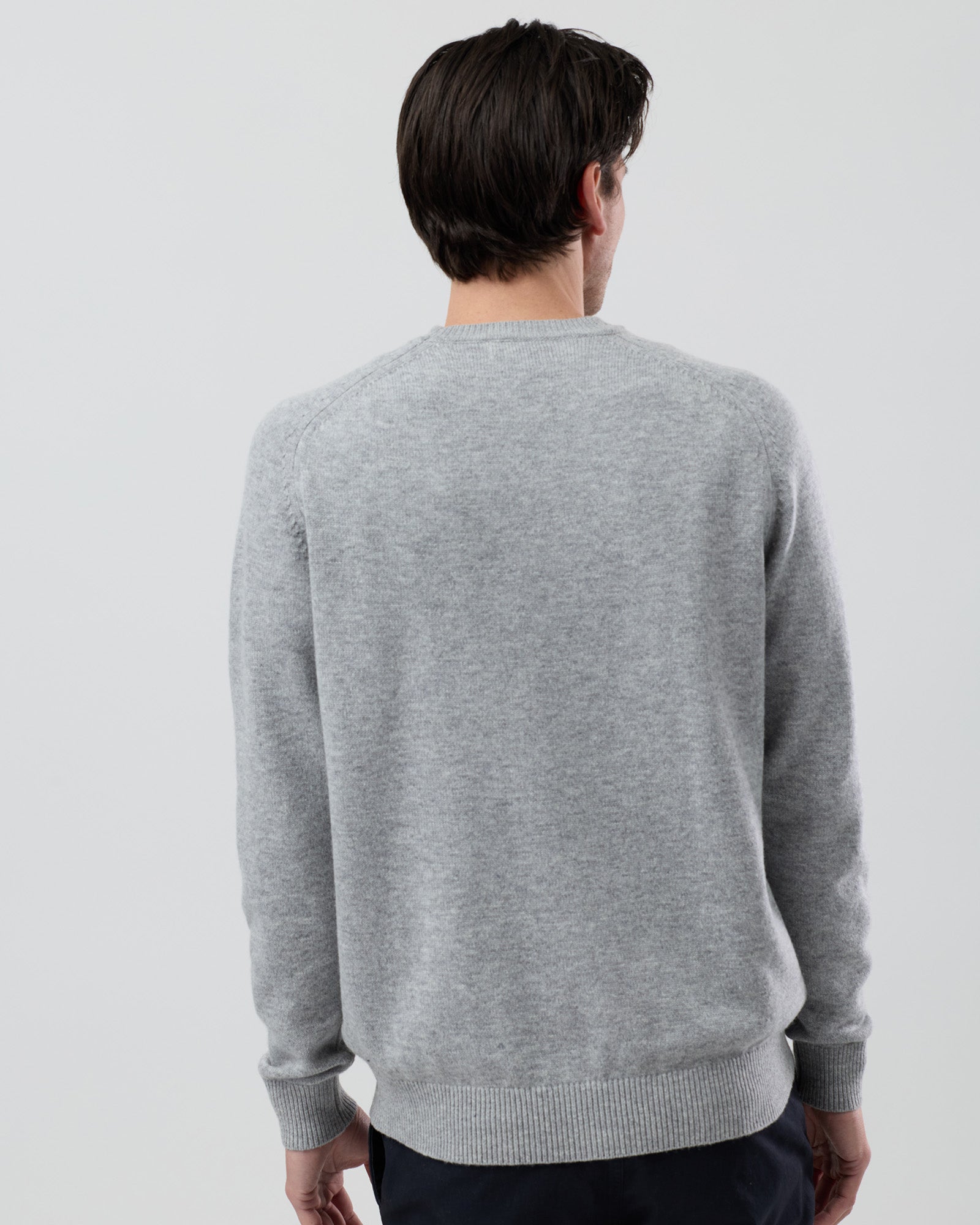 Rear view of a men's light grey wool blend crew neck sweater highlighting the saddle shoulder design and clean silhouette on a grey background.