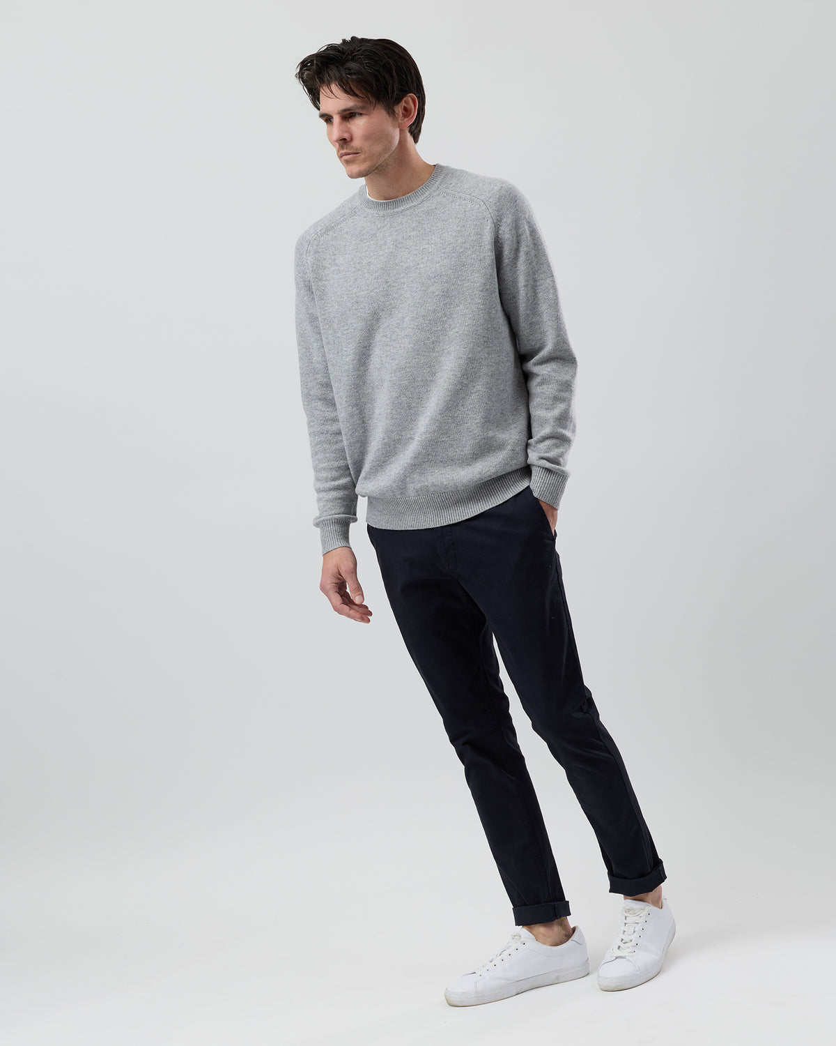 Full-length side profile of a men's light grey wool blend crew neck knit paired with navy chinos against a grey background.