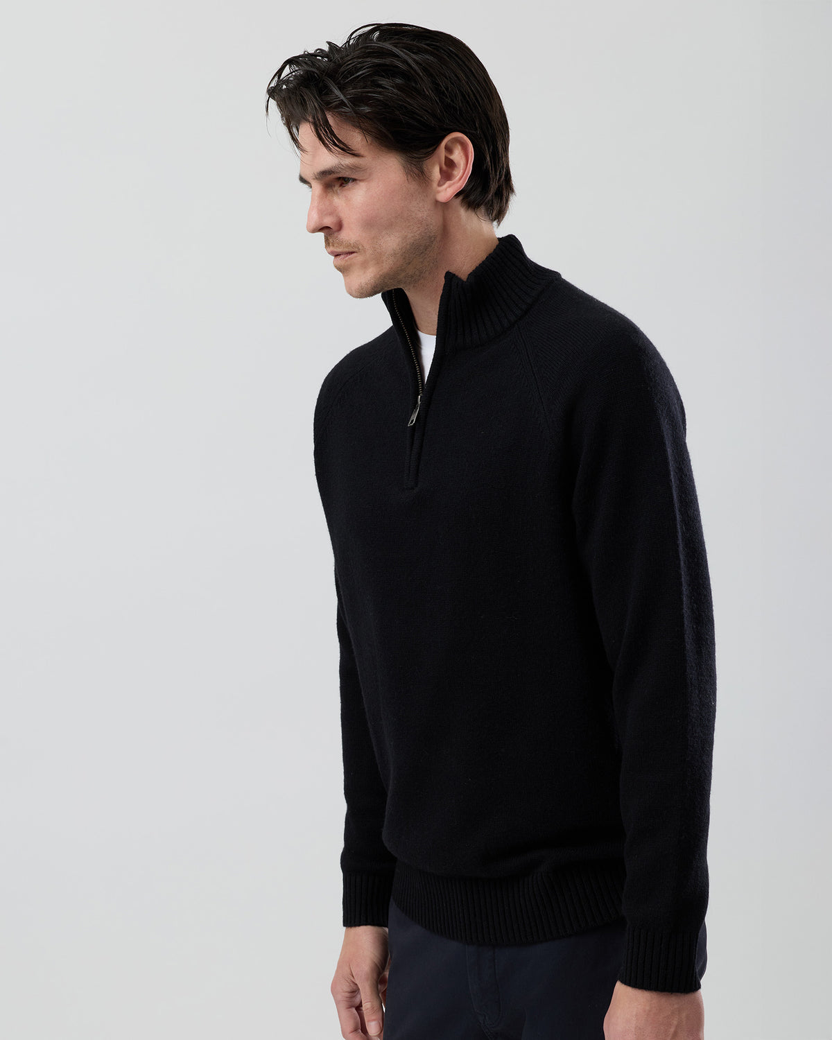 Angled side view of a men's black wool blend quarter zip knit showing the streamlined silhouette and premium jersey knit construction.