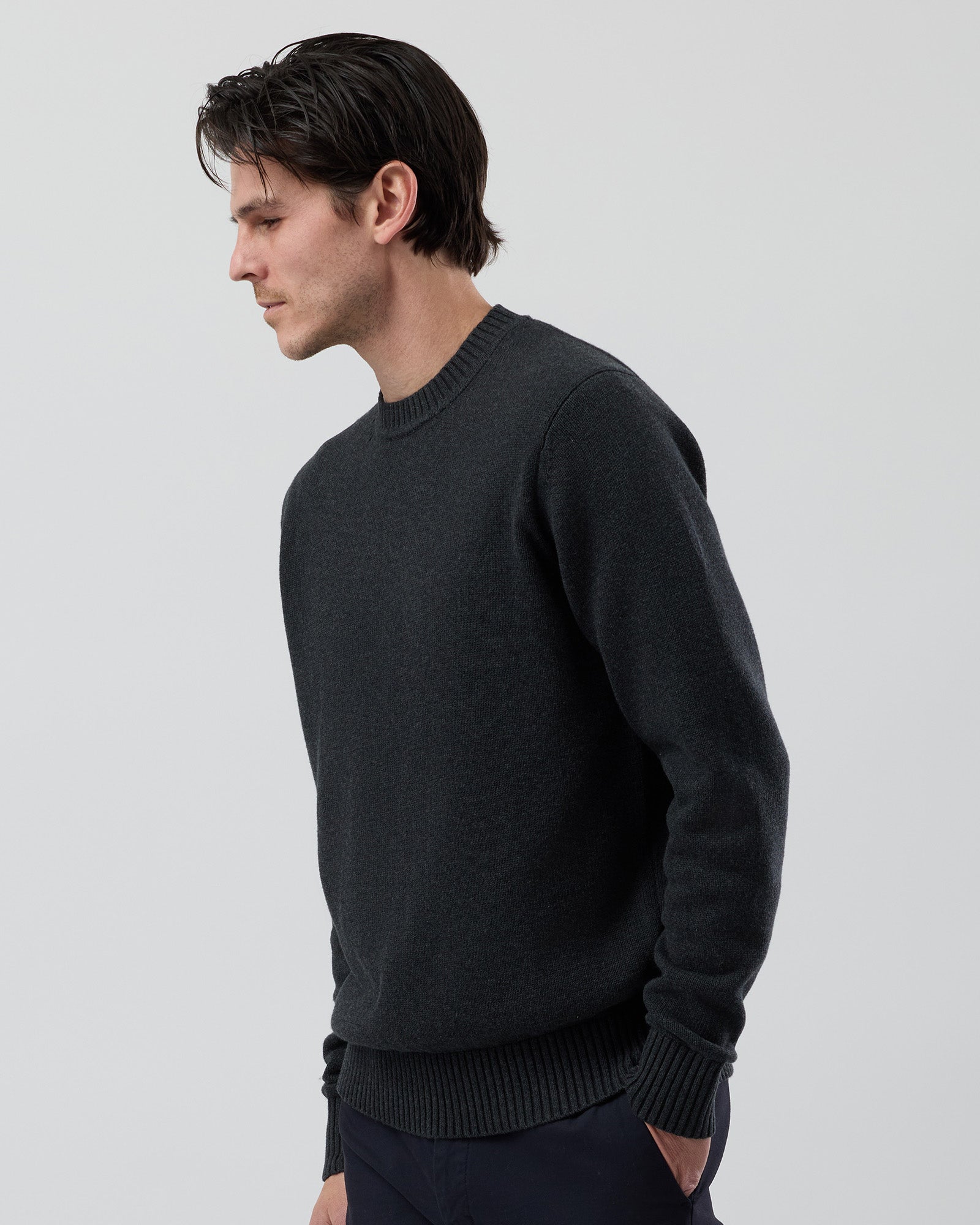 Angled side view of the Wayver charcoal 100% cotton crew neck knit showing the tailored sleeve shape and premium cotton construction.