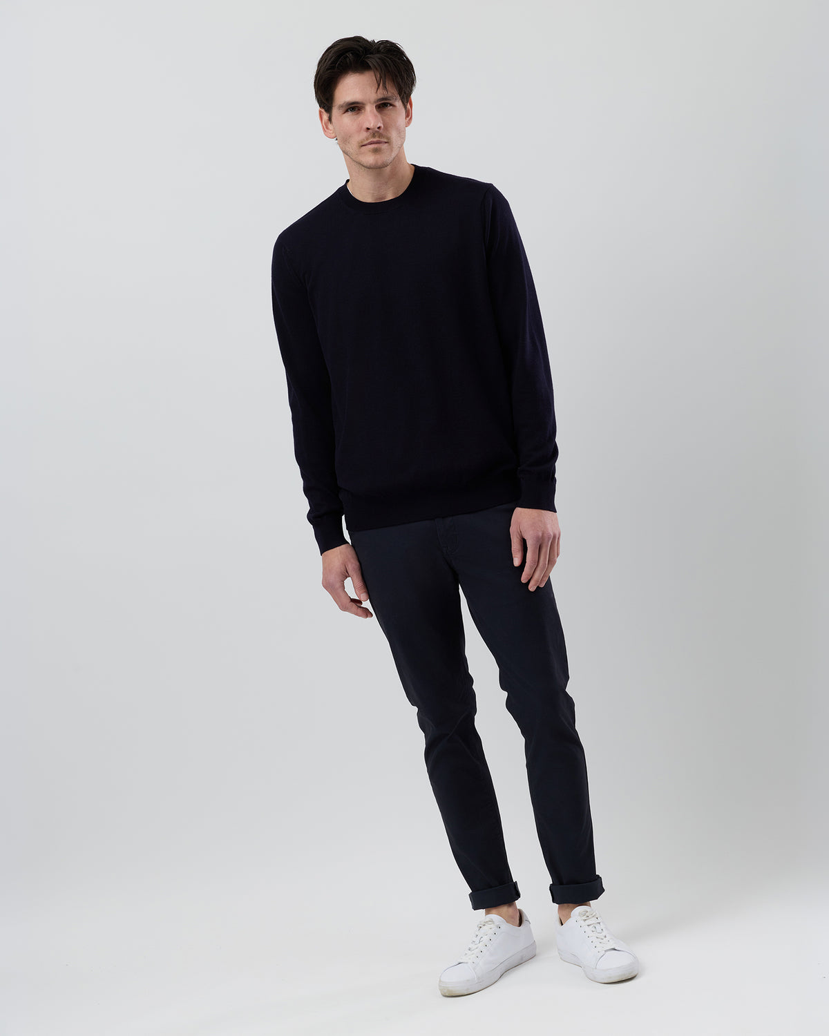 Full-length front view of a male model wearing a Wayver Originals navy Australian ultrafine merino crew neck knit styled with navy chinos on a grey background.