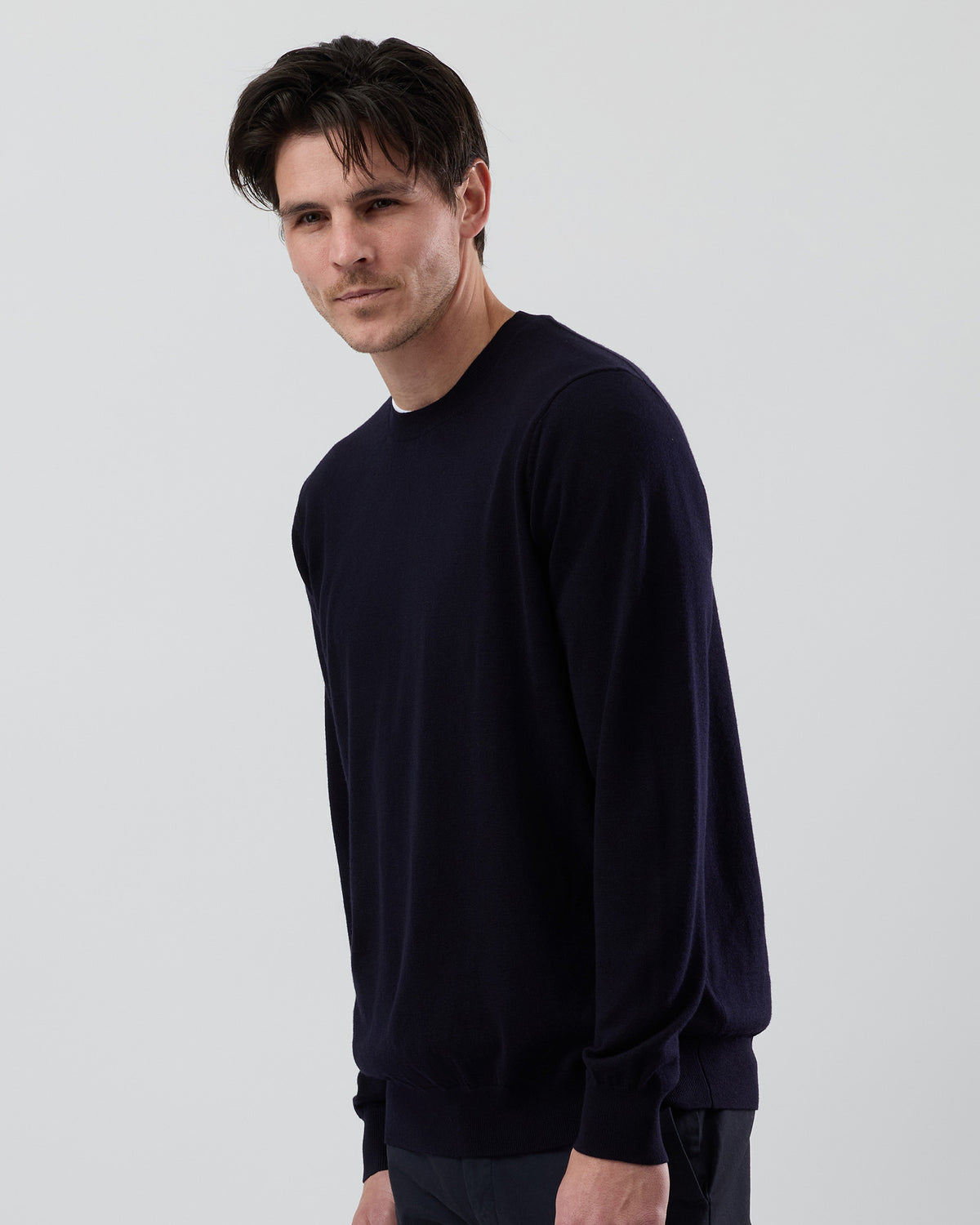 Side angle of a men's navy Australian ultrafine merino crew neck sweater, highlighting the tailored fit and premium knit fabric against a grey background.