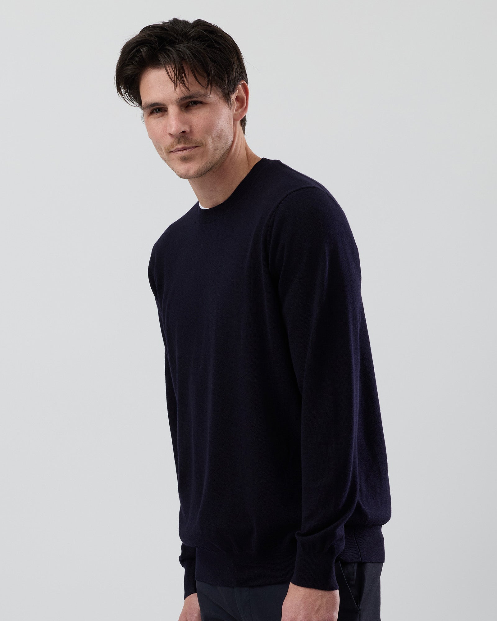 Side angle of a men's navy Australian ultrafine merino crew neck sweater, highlighting the tailored fit and premium knit fabric against a grey background.