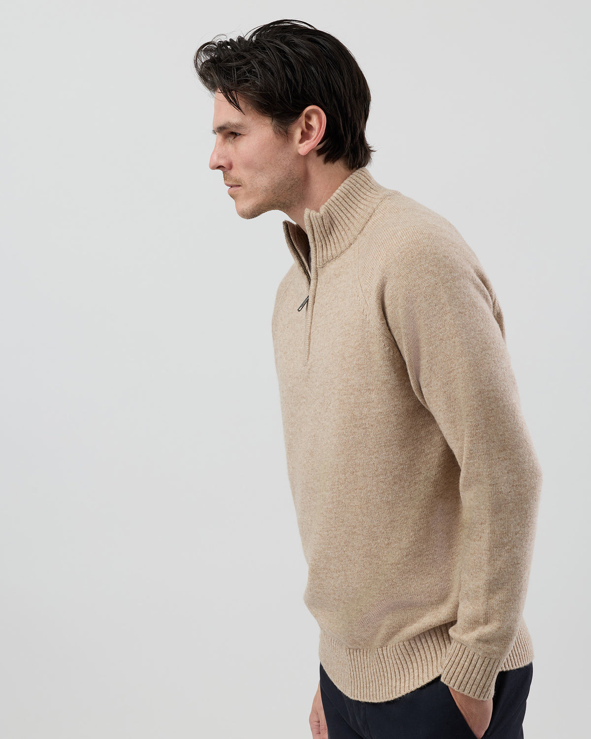 Angled side view of a men's oatmeal wool blend quarter zip knit showing the refined silhouette and premium jersey knit texture.
