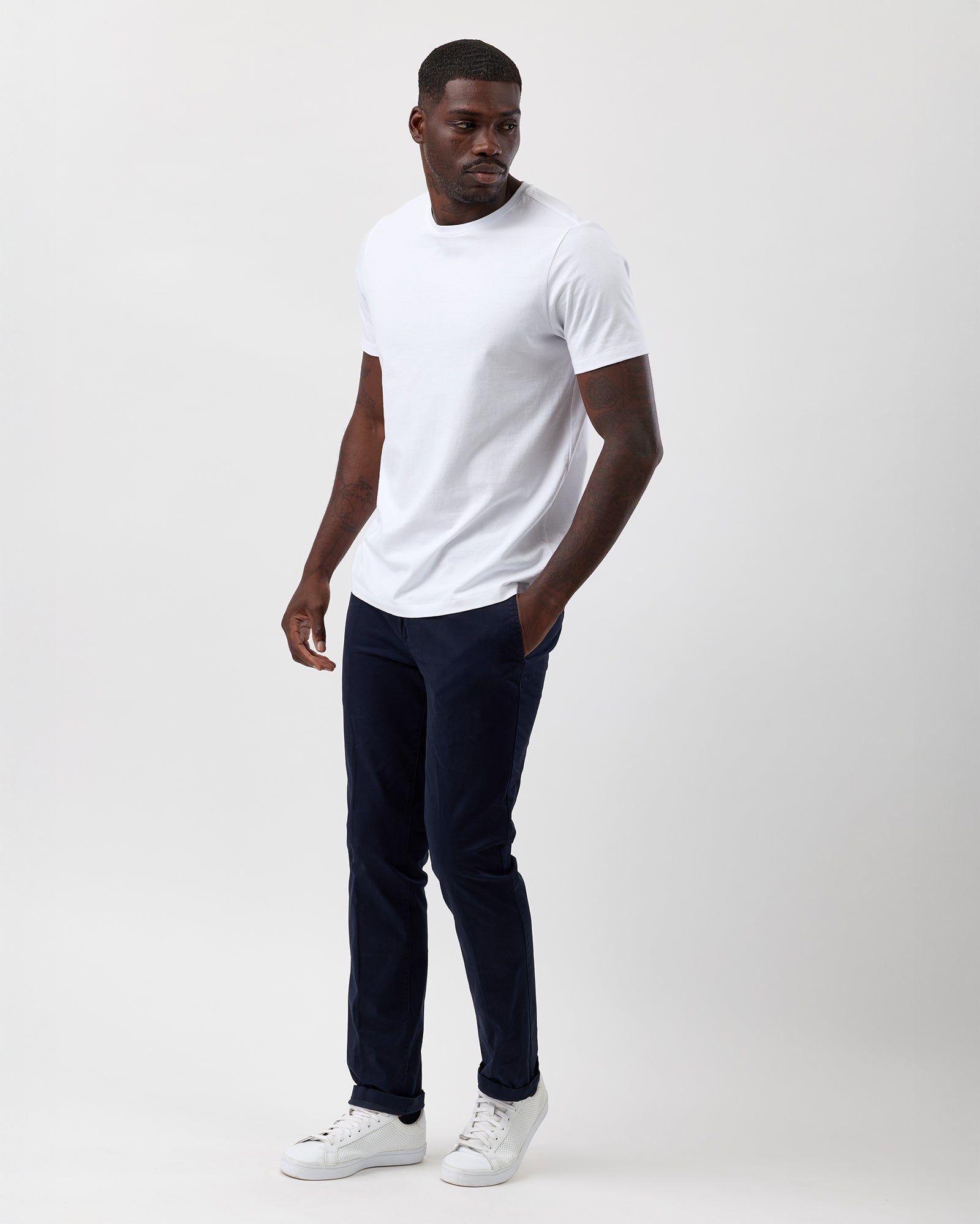 Man wearing a white t-shirt, navy cotton stretch chino pants, and white sneakers on a plain background, street styled, full body shot