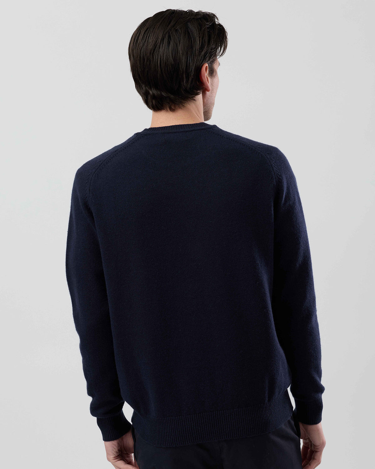Rear view of a men's navy wool blend crew neck sweater highlighting the clean silhouette and saddle shoulder construction on a grey background.