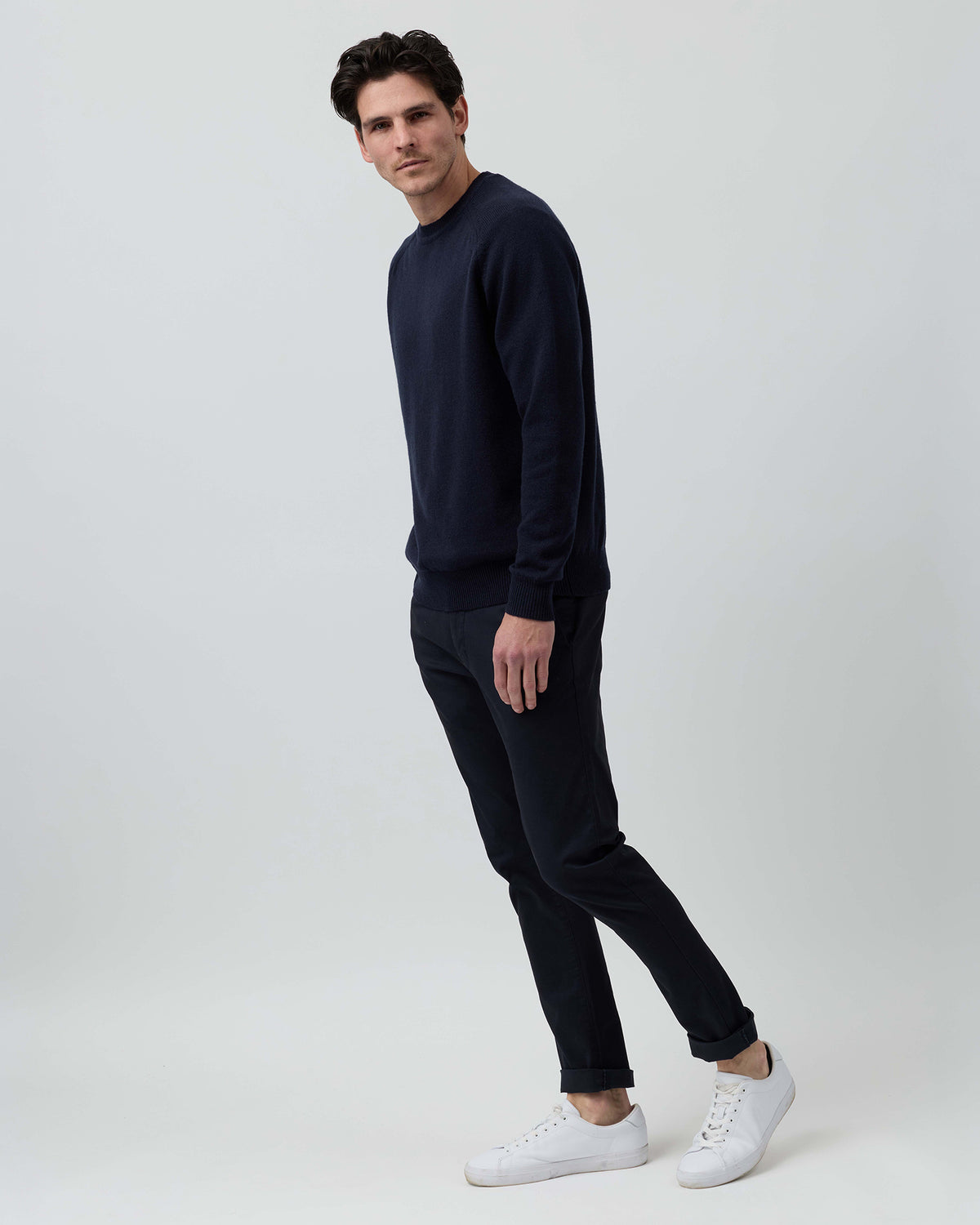 Full-length side profile of a men's navy wool blend crew neck knit styled with navy chinos on a grey background.